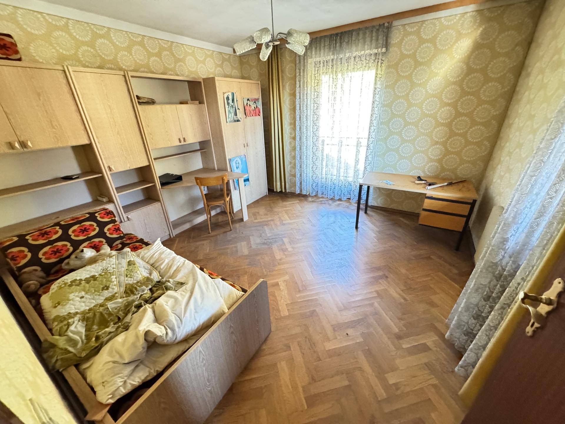 Schlafzimmer mit Parkettboden, Schränken und einem Bett, beleuchtet durch ein großes Fenster.