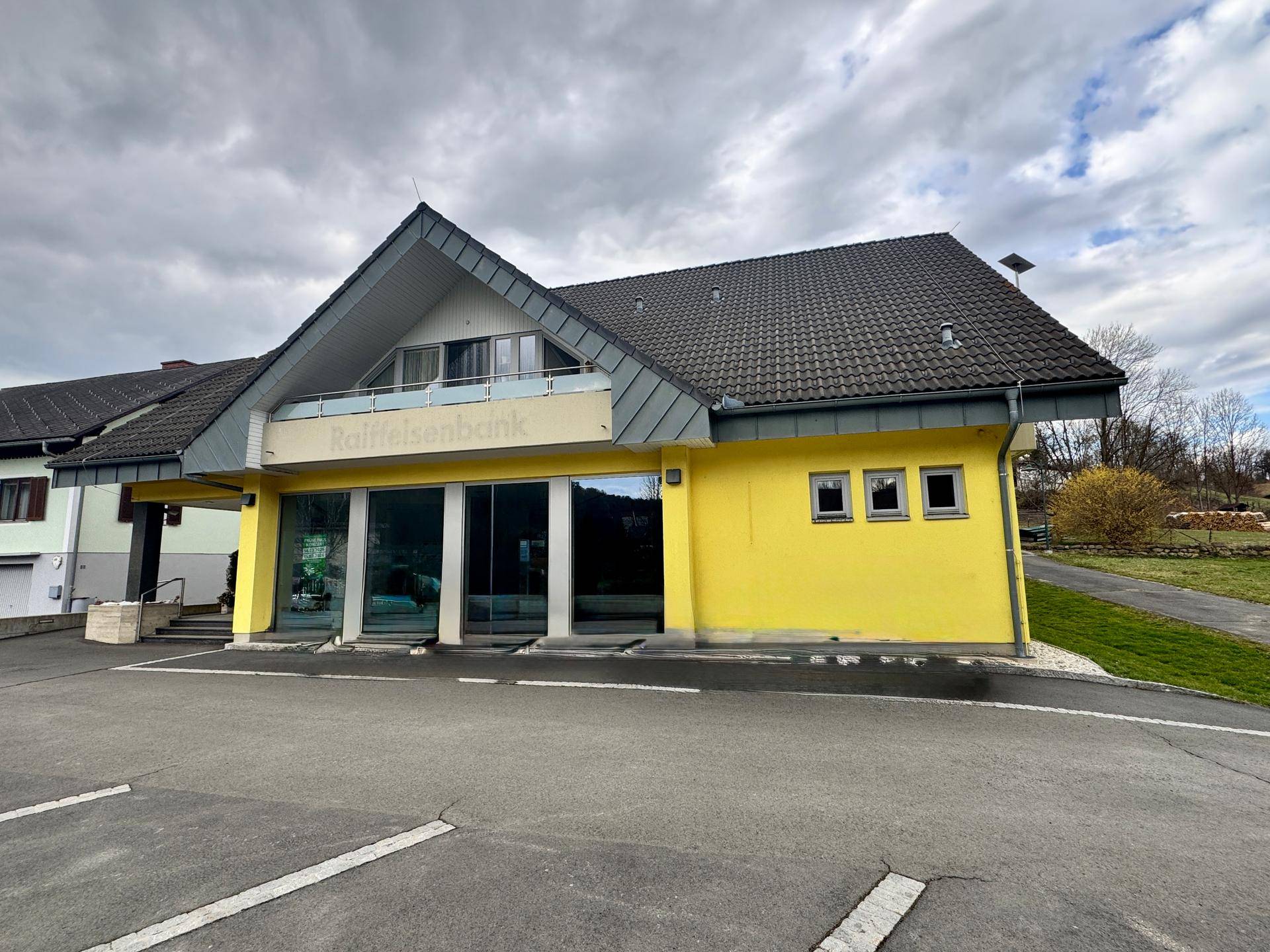 Frontale Ansicht des gelben Gebäudes mit Parkplatz und großen Fenstern.