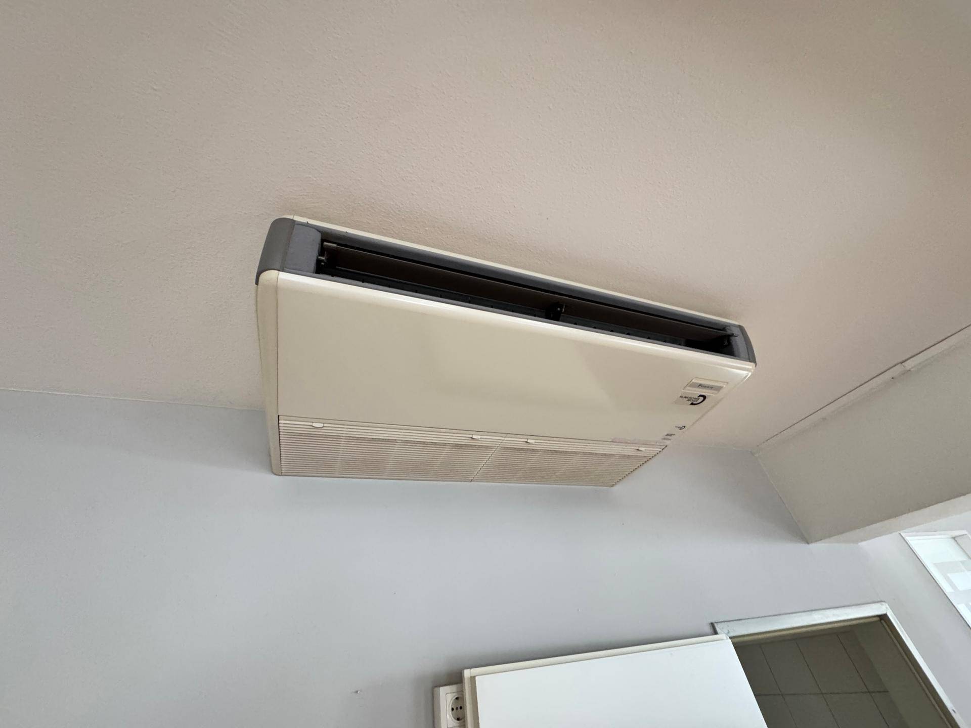 Deckenmontierte Klimaanlage in einem Raum mit weißer Decke und grauen Wänden.
