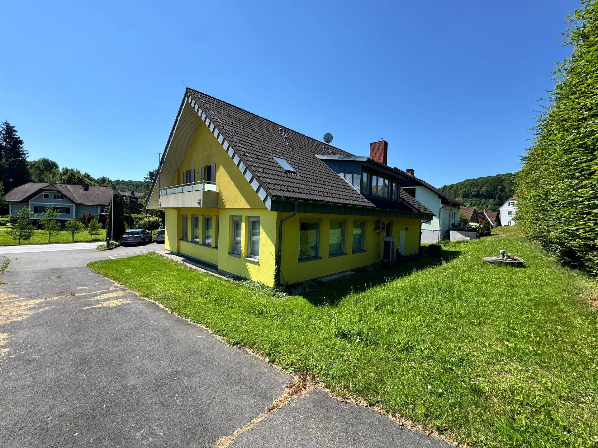 Seitenansicht des gelben Hauses mit Satteldach, Balkon und Blick auf die ländliche Umgebung.