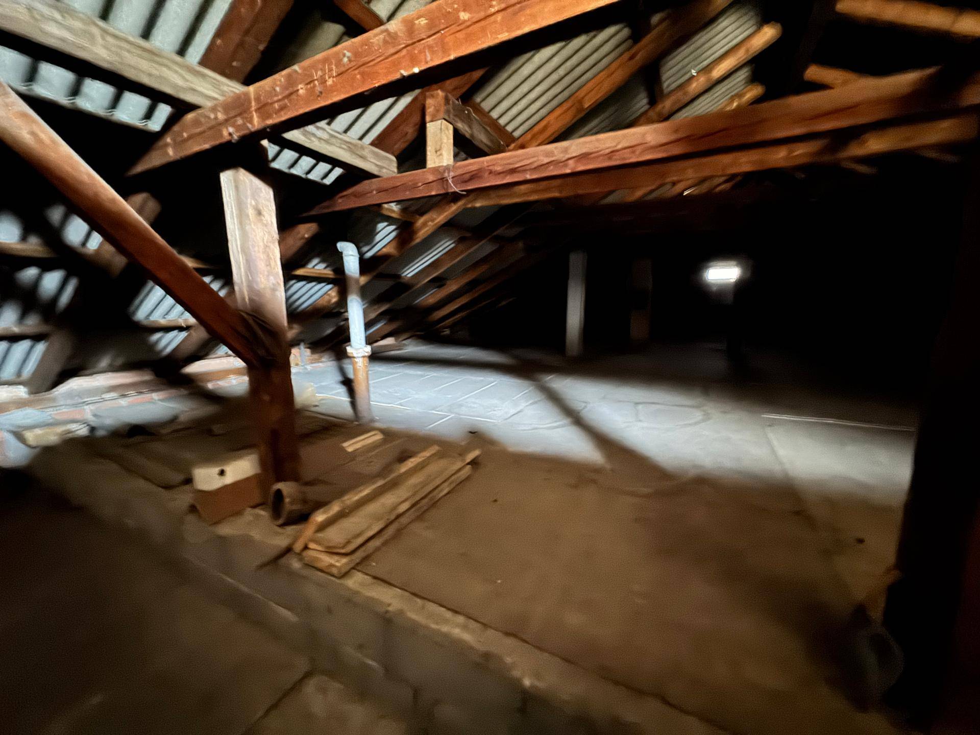 Dunkler Dachboden mit sichtbaren Holzbalken und unfertiger Dachkonstruktion, ideal als Stauraum.