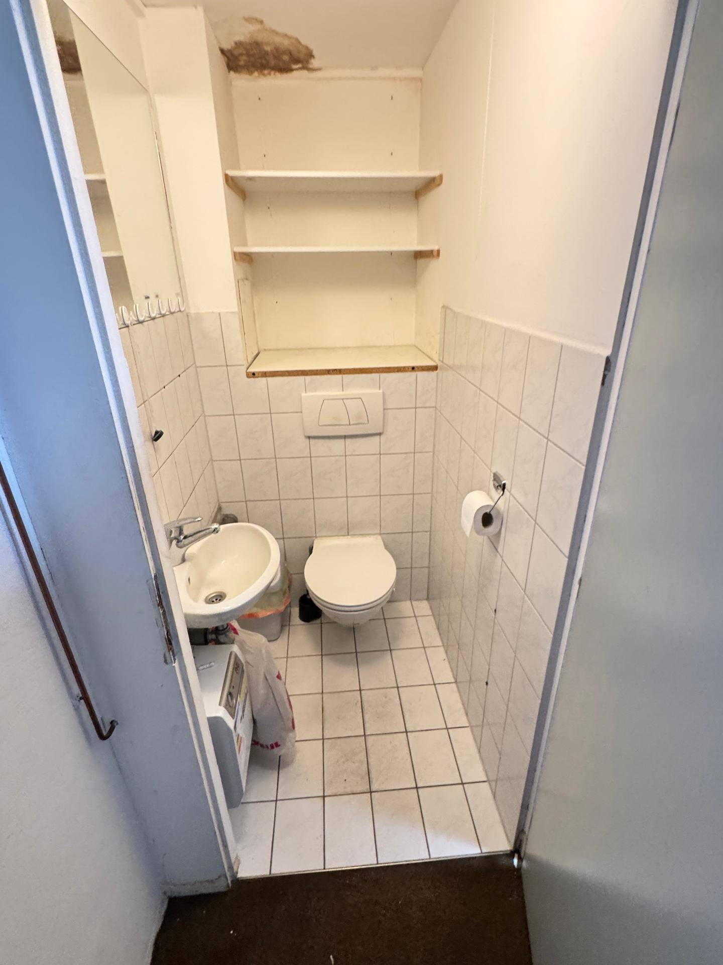 Kleine Gästetoilette mit Fliesenboden, Waschbecken und Wand-WC.