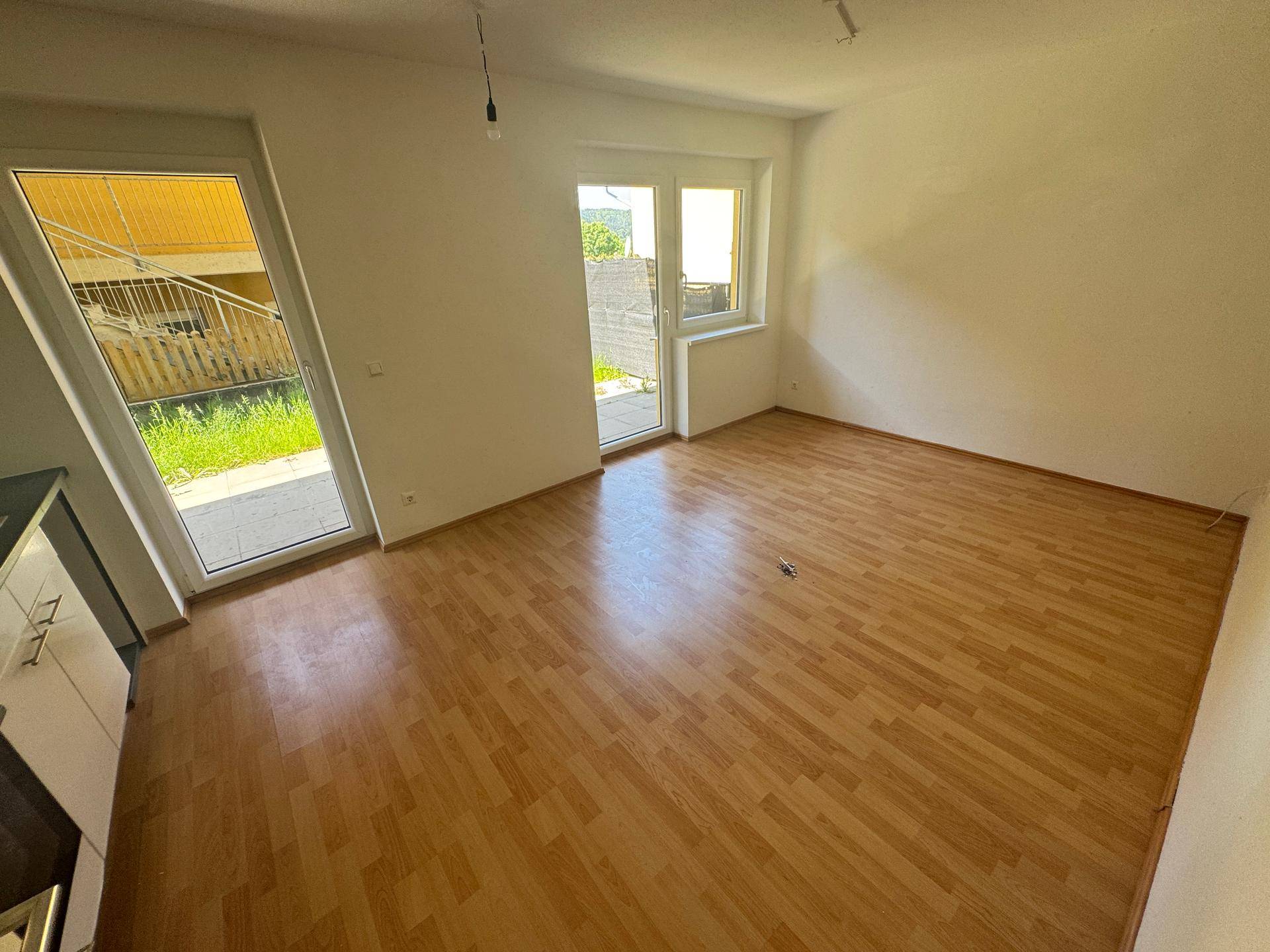 Heller Wohnbereich mit Laminatboden und großen Fenstern, die Zugang zum Außenbereich bieten.