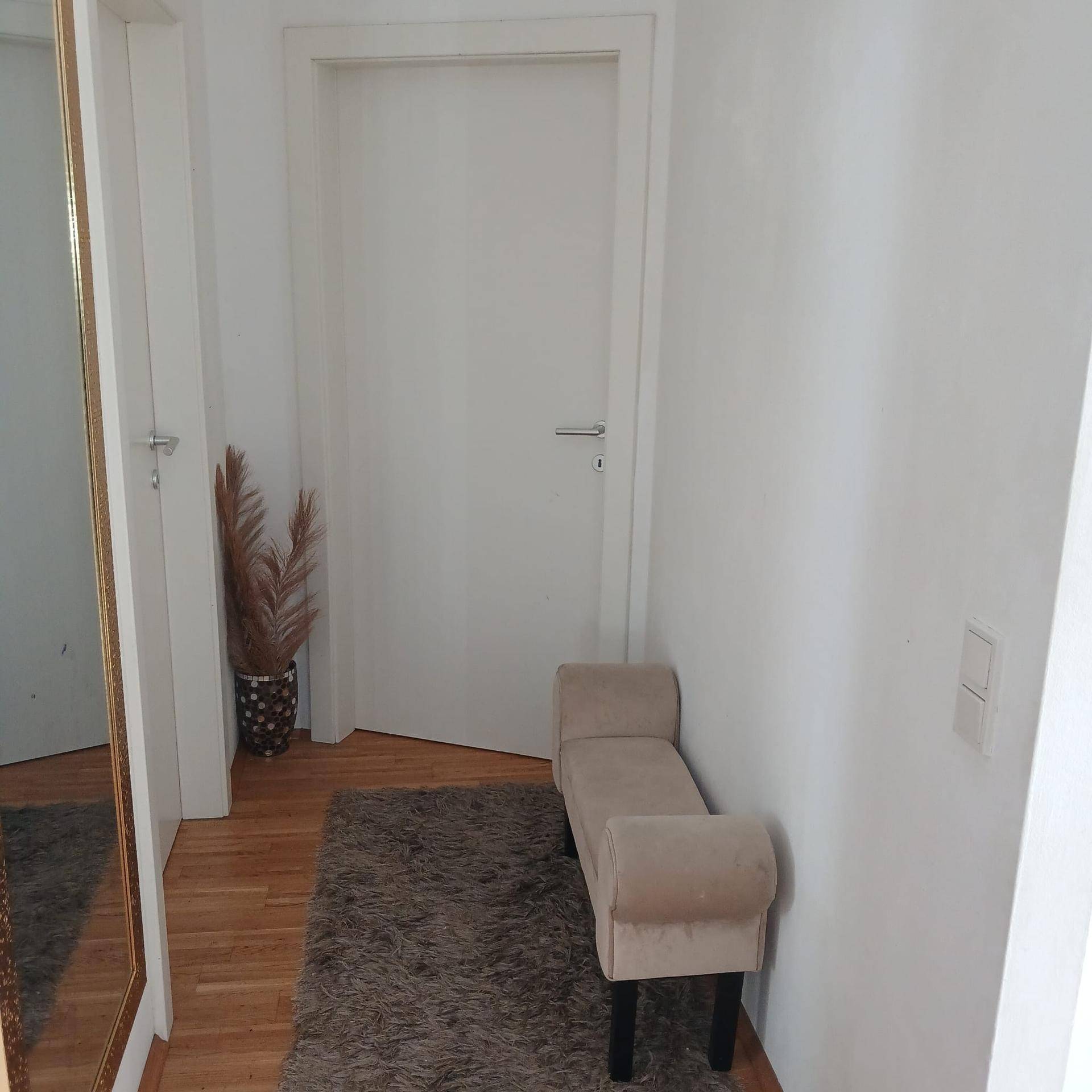 Heller Flur mit Holzboden, einem kleinen Sitzbereich und einem großen Spiegel.