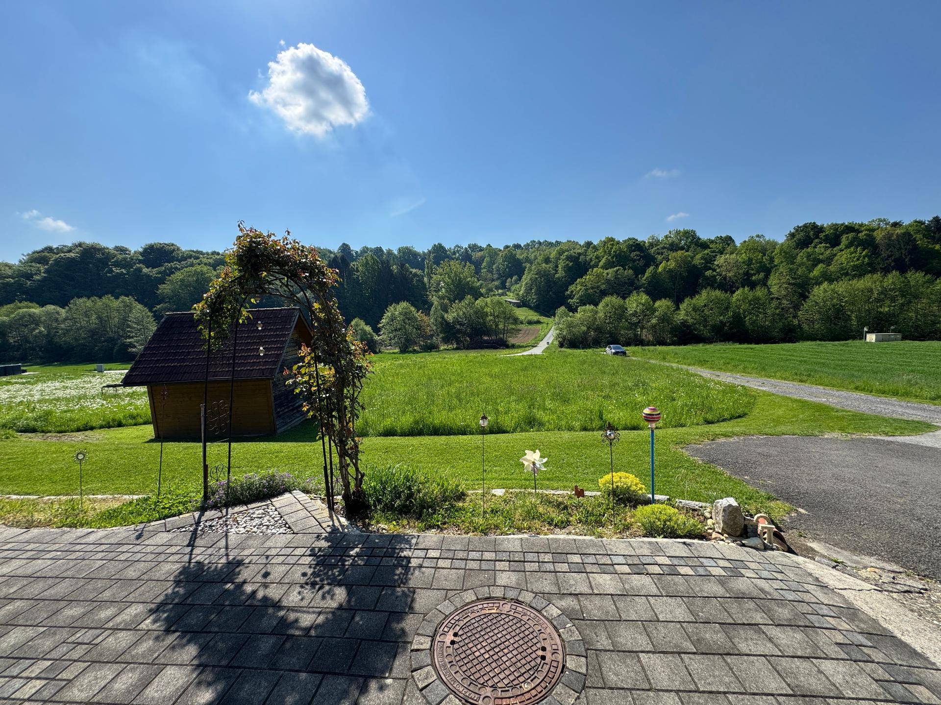 Gepflasterte Terrasse mit Rosenbogen und weitem Blick über grüne Felder und Landschaft.