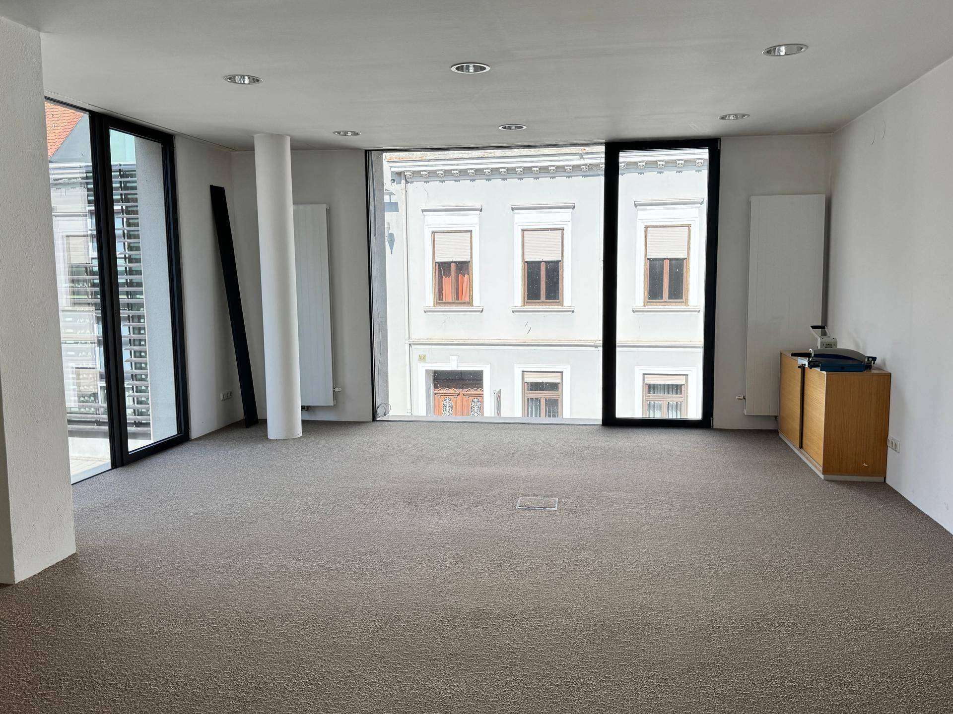 Geräumiges Büro mit großen Fenstern und Teppichboden, bietet einen weiten Blick auf die Umgebung und viel Licht.