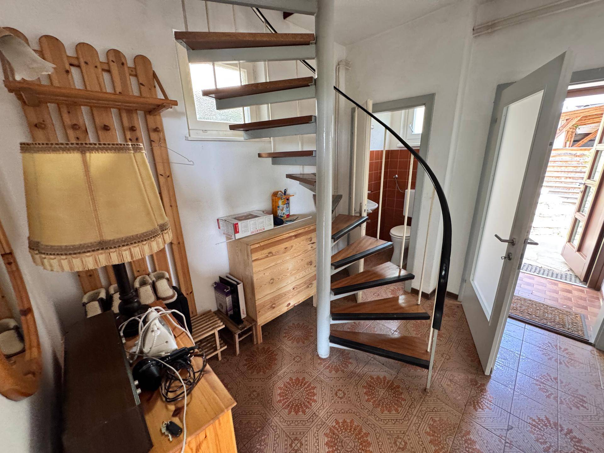Flur mit Wendeltreppe, gemustertem Boden und Zugang zum Außenbereich.