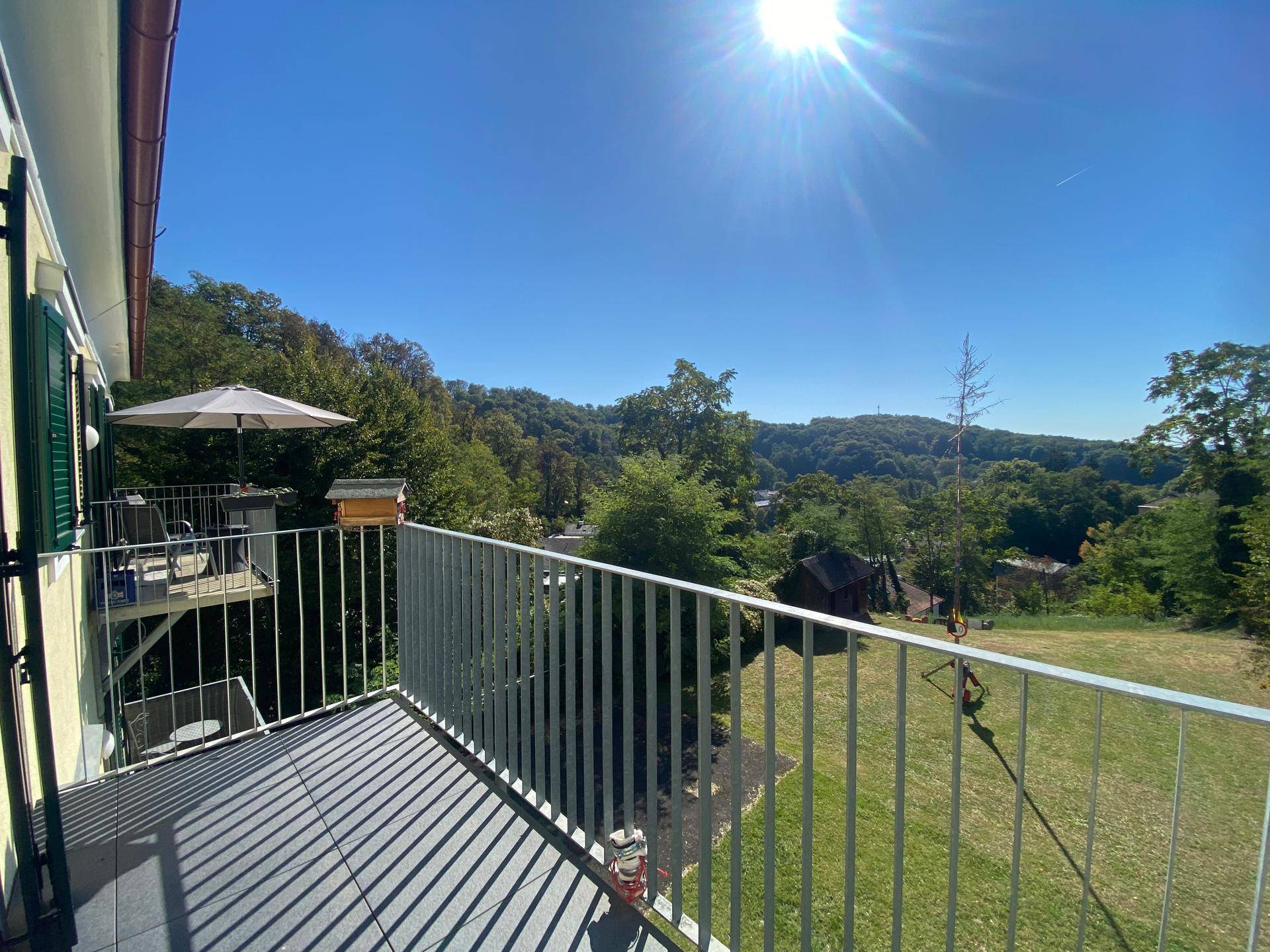 Großer Sonnenbalkon mit Fliesenboden und atemberaubendem Panoramablick ins Grüne.
