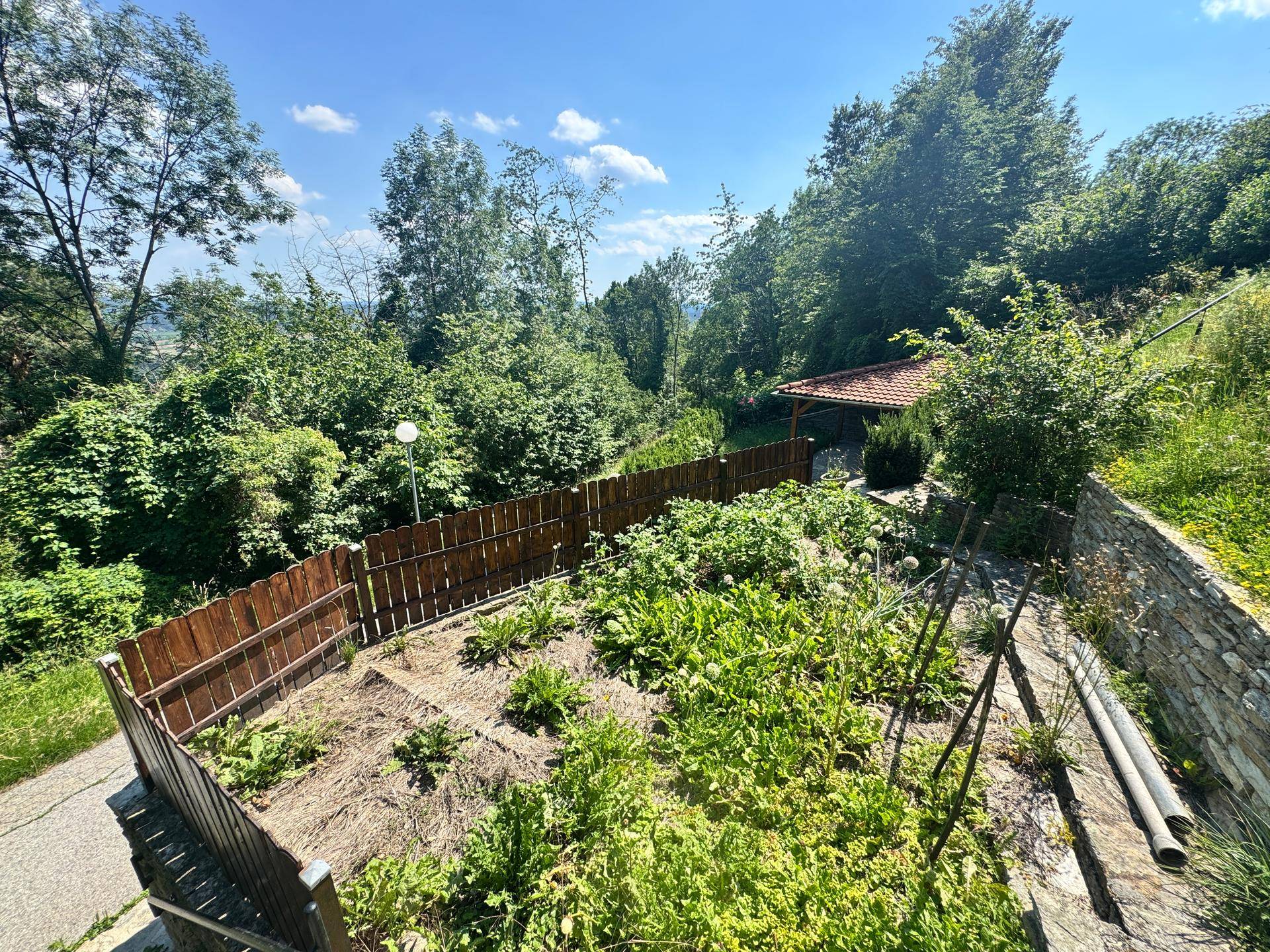 Ein gepflegter Gemüsegarten mit Holzzaun und Blick auf die umliegende grüne Landschaft.