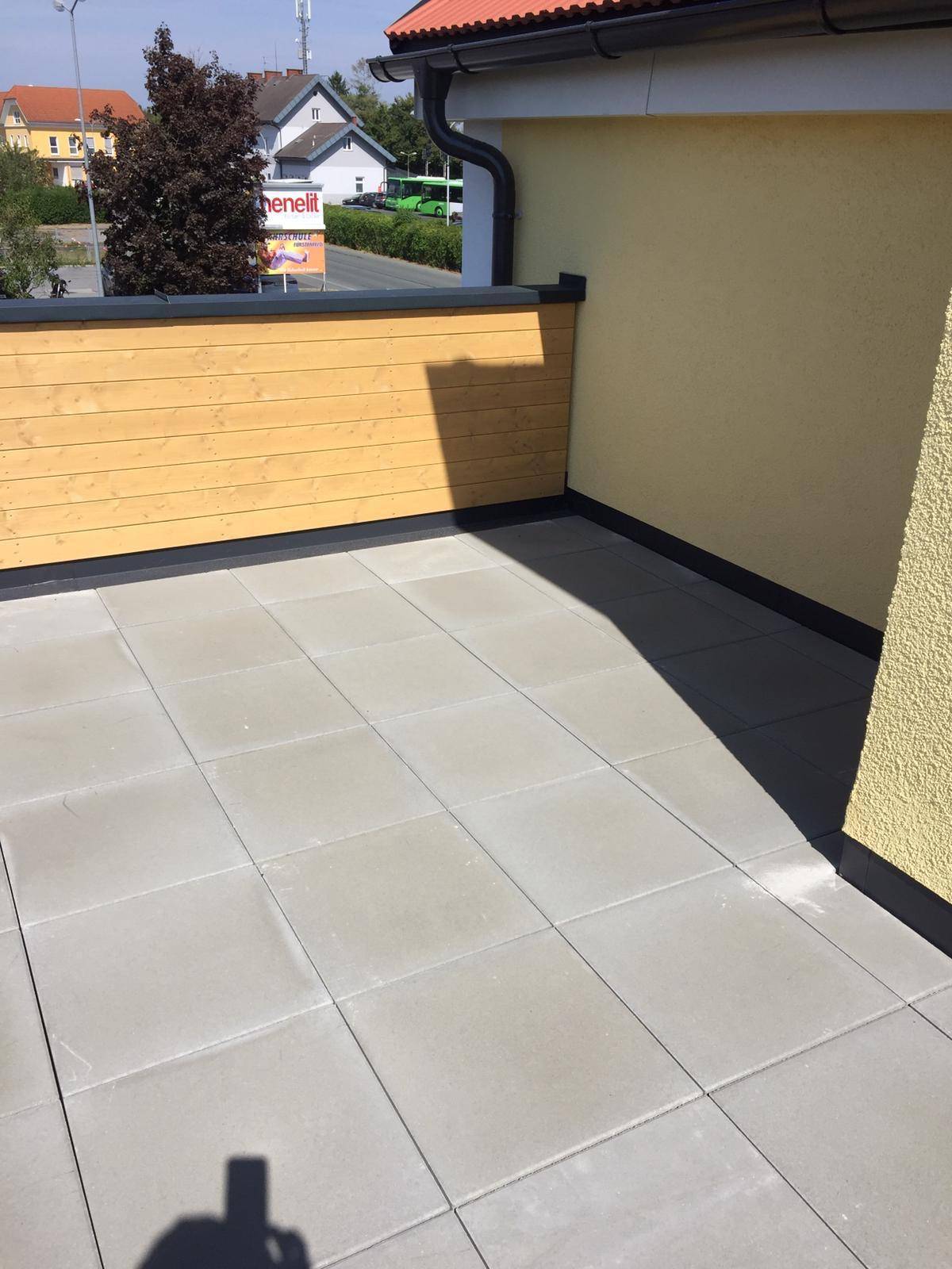 Helle Terrasse mit großen Fliesen und Holzsichtschutz, ideal für entspannte Stunden.