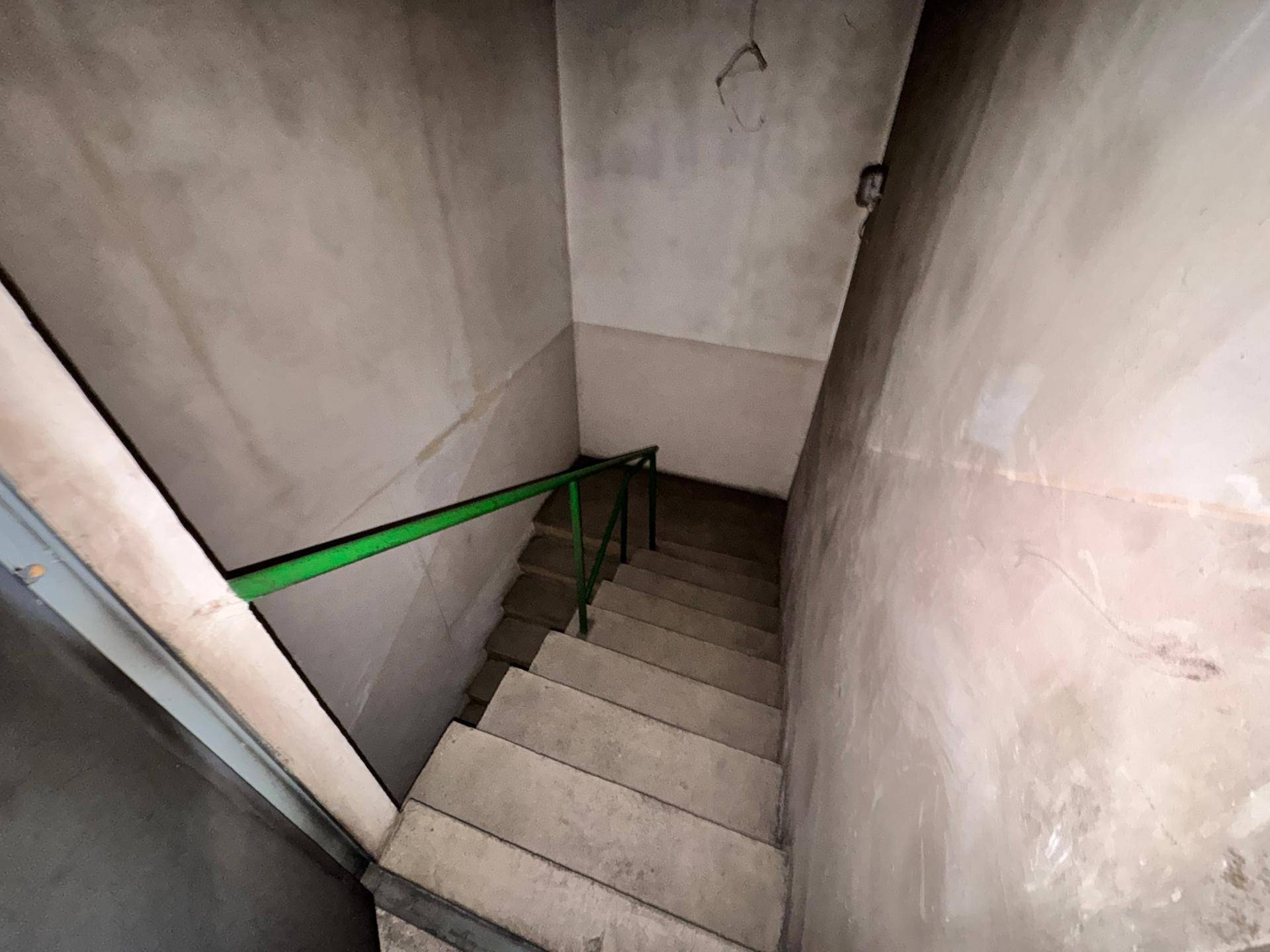 Betontreppe mit grünem Metallgeländer, die in einen Kellerraum führt.