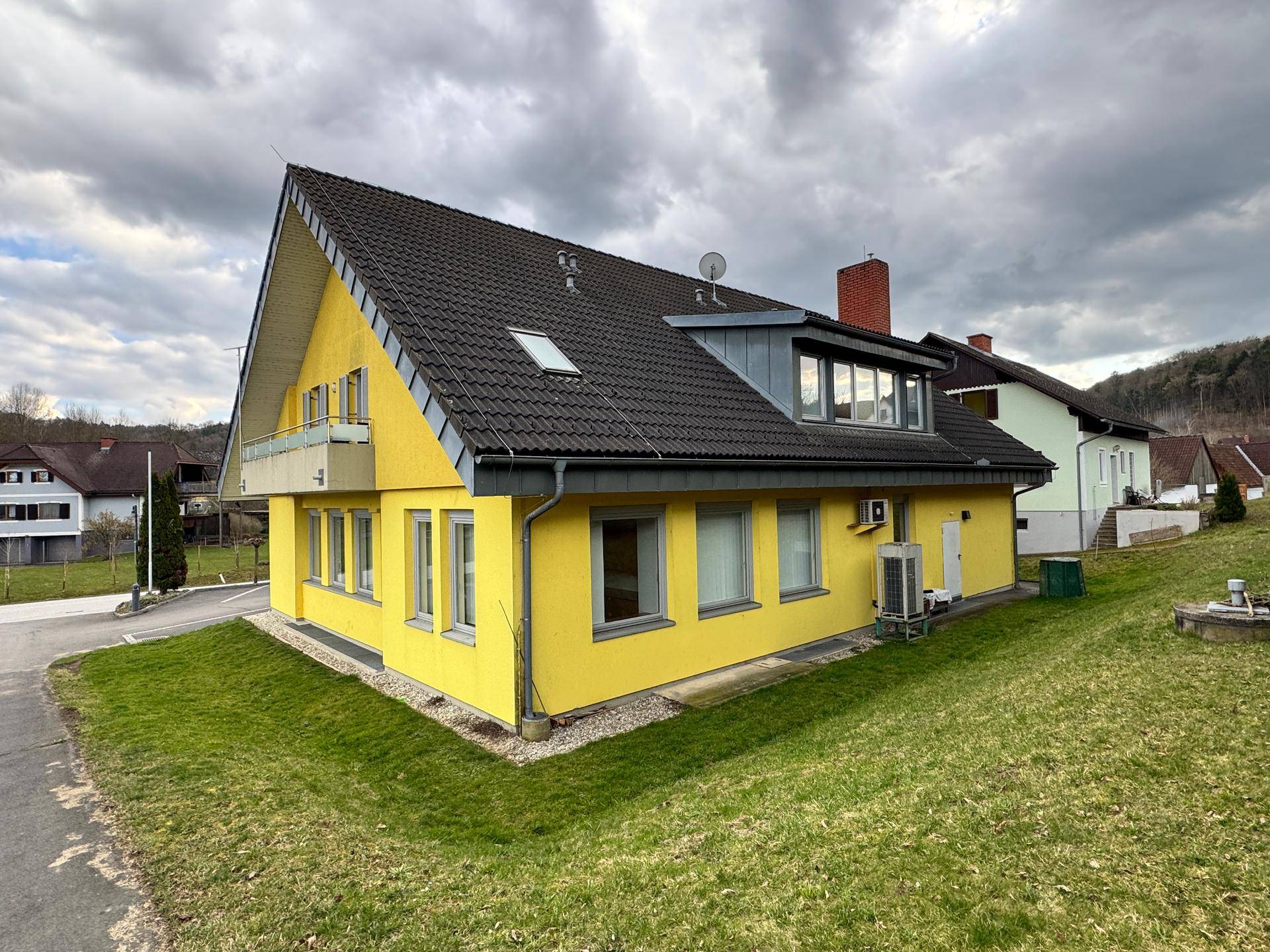 Seitenansicht des gelben Gebäudes mit Rasenfläche und Dachfenstern.
