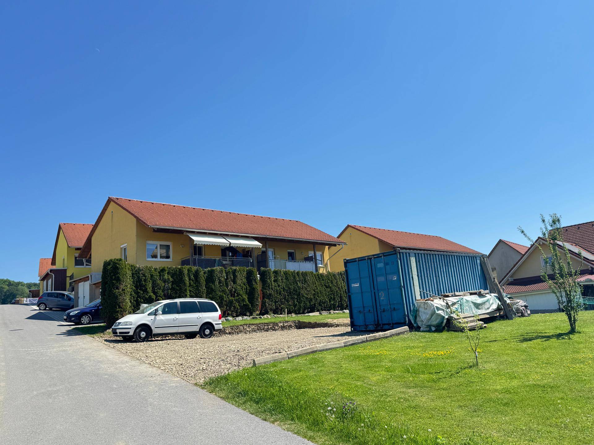 Reihen von Wohngebäuden mit gepflegter Hecke und einem blauen Container auf einer Grünfläche.