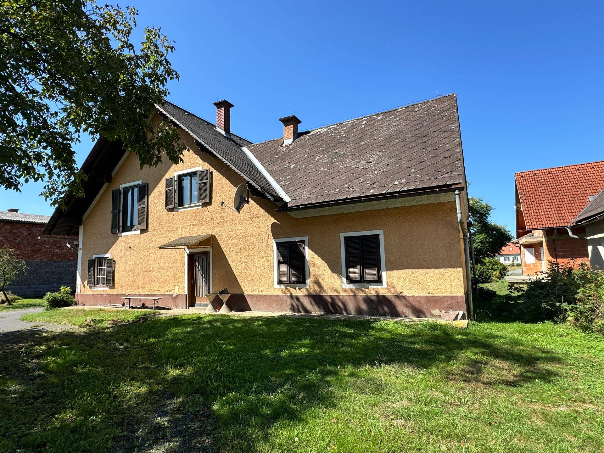 Landhaus mit gelber Fassade, dunklen Fensterläden und großem Gartenbereich unter blauem Himmel.