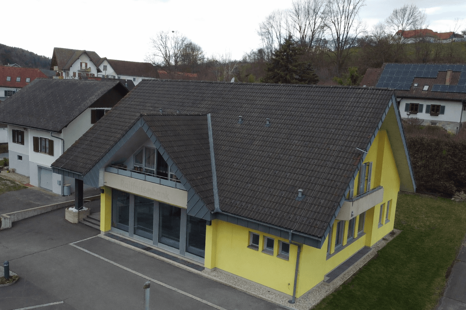Luftaufnahme des gelben Gebäudes mit Satteldach und umliegenden Wohnhäusern in ländlicher Umgebung.