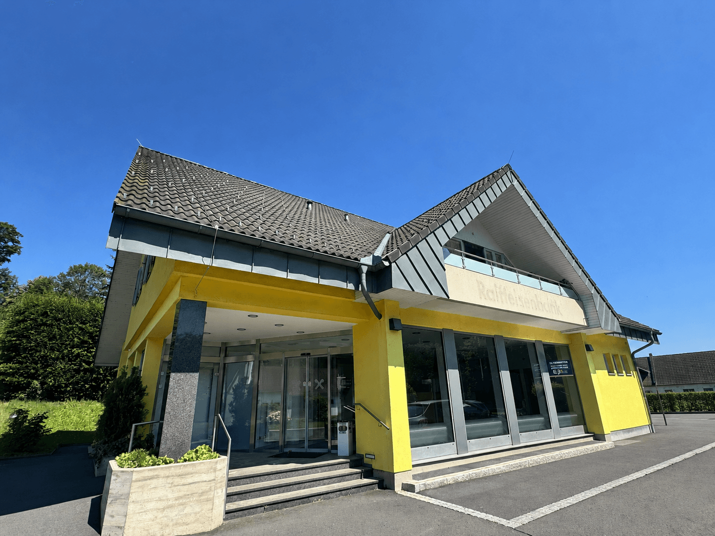 Gelbes Bankgebäude mit markantem Dach und großzügigem Eingangsbereich unter blauem Himmel.