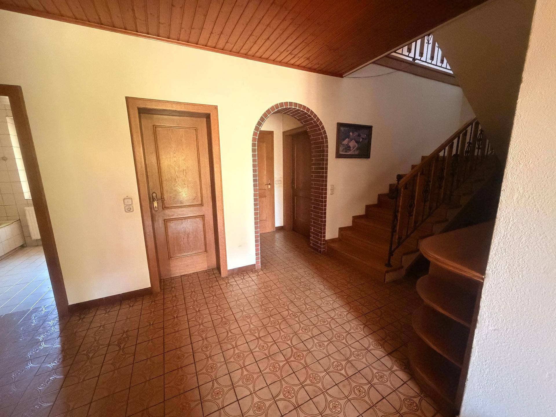 Eingangsbereich mit gefliestem Boden, Holztreppe und Holztüren im traditionellen Stil.