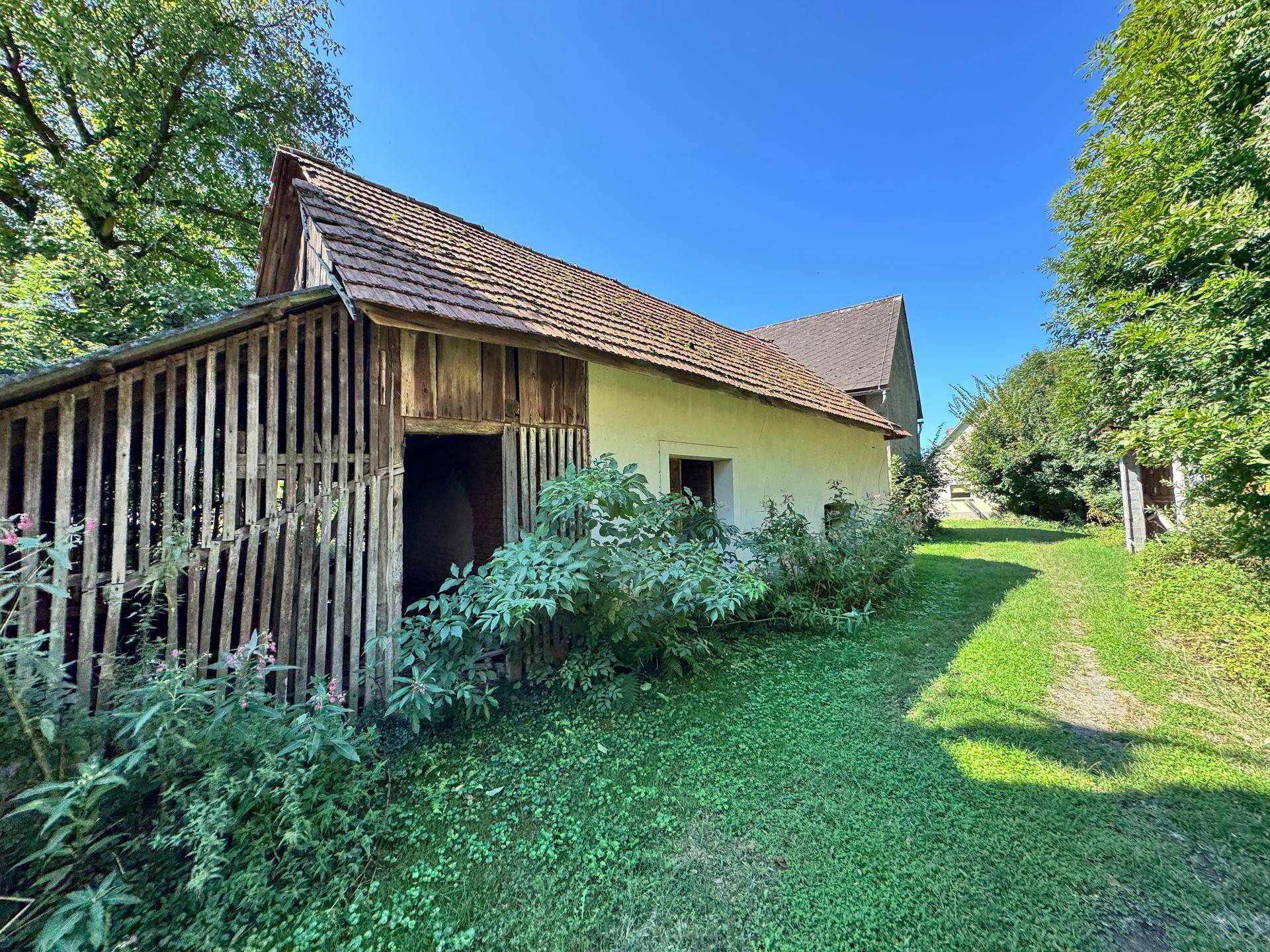 Ländliches Nebengebäude mit Holzlattung und Ziegeldach, umgeben von Grün.