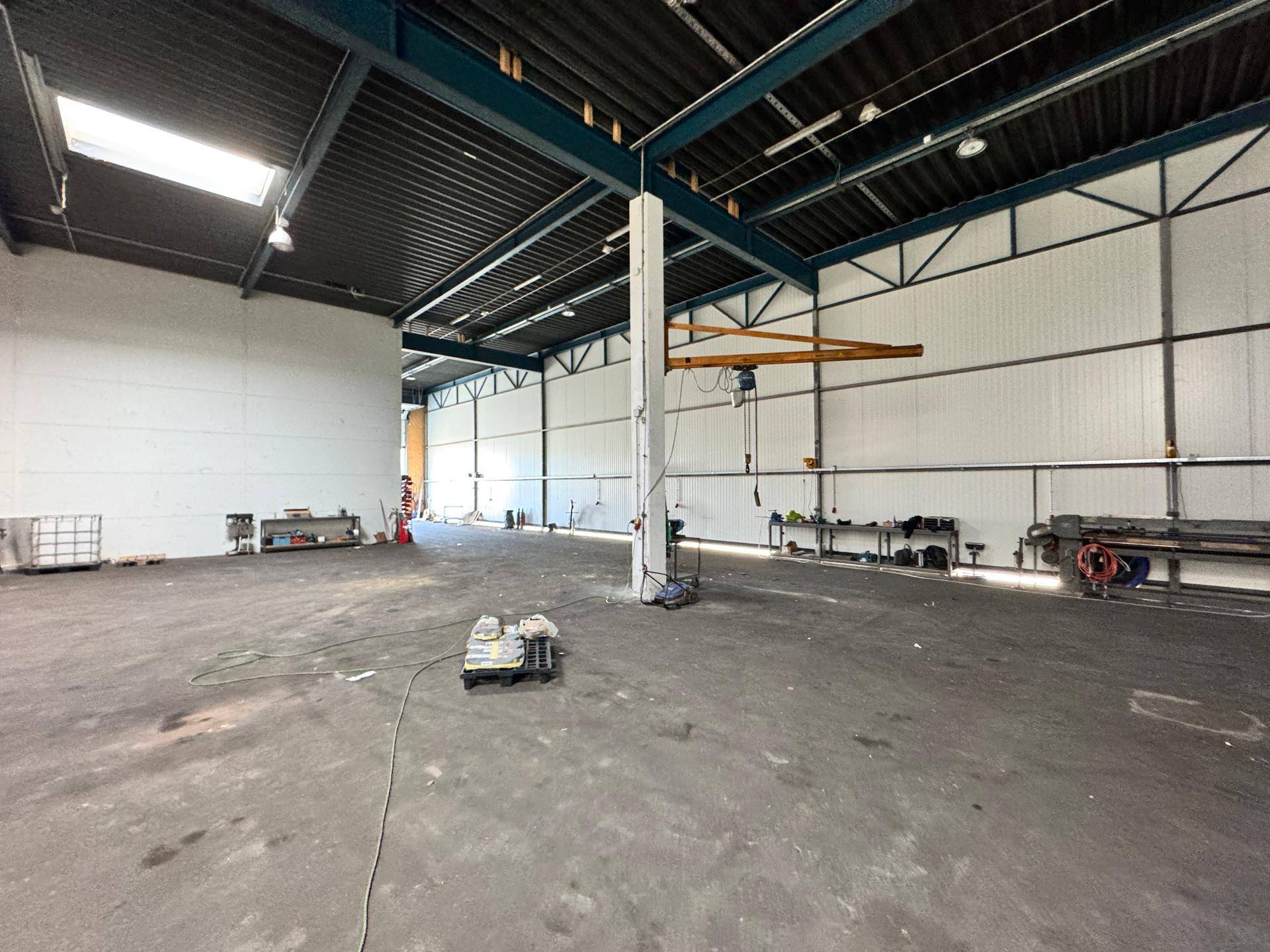 Weitläufige Industriehalle mit hohen Decken, Stahlträgern und einem Kran an der Decke.