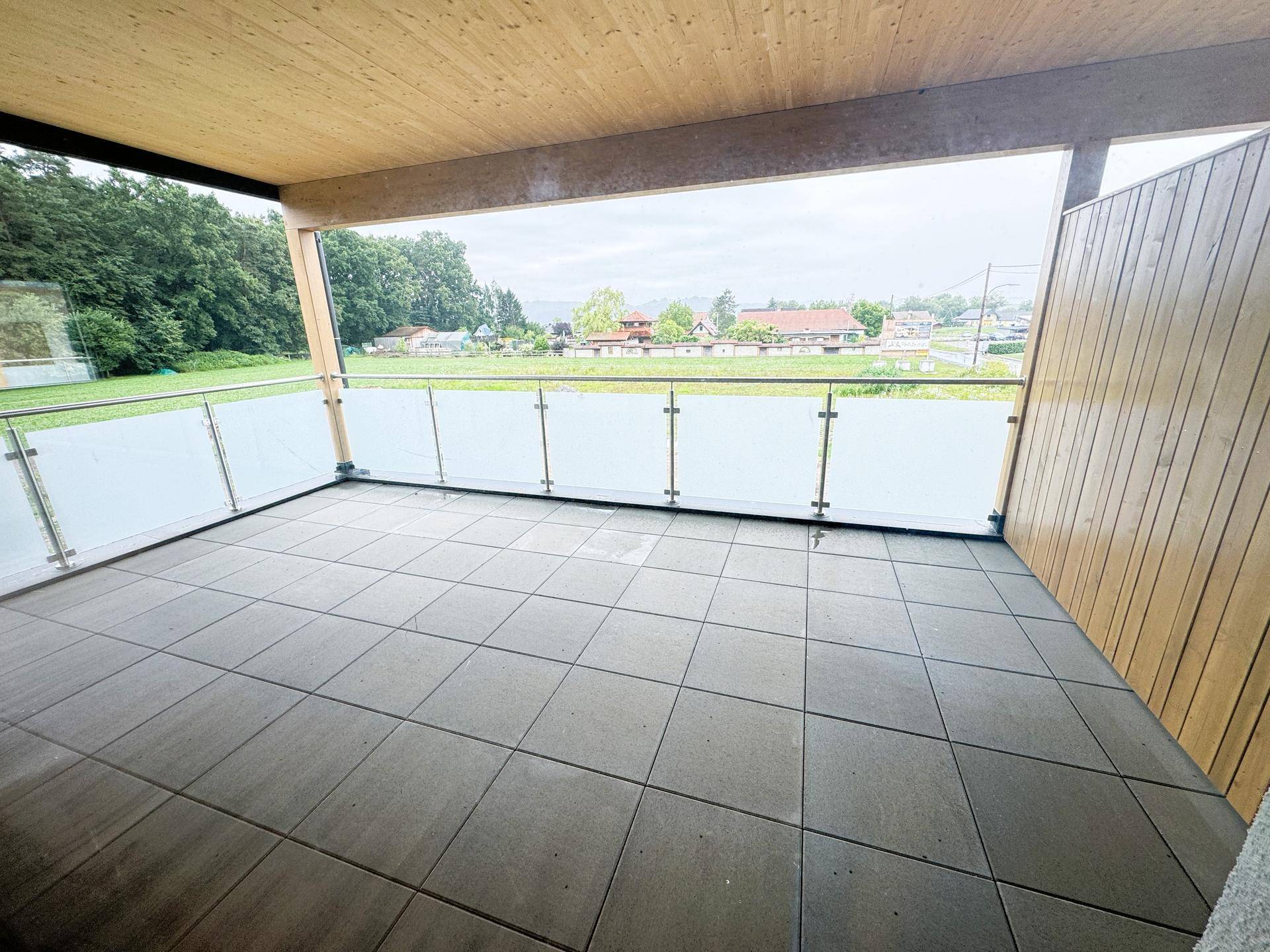 Geräumiger Balkon mit Fliesenboden, Glasgeländer und Blick auf die ländliche Umgebung.