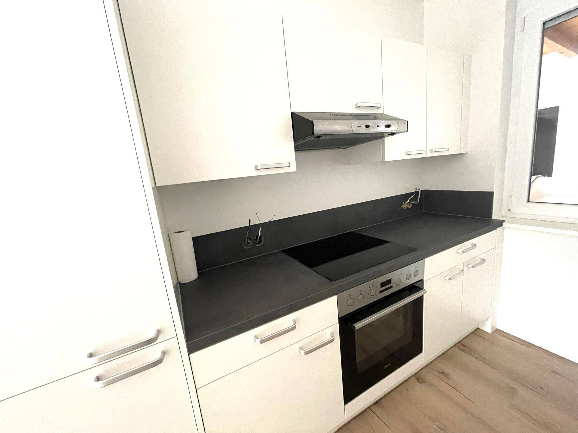 Moderne Einbauküche mit weißen Hochglanzfronten, dunkler Arbeitsplatte und Induktionskochfeld.
