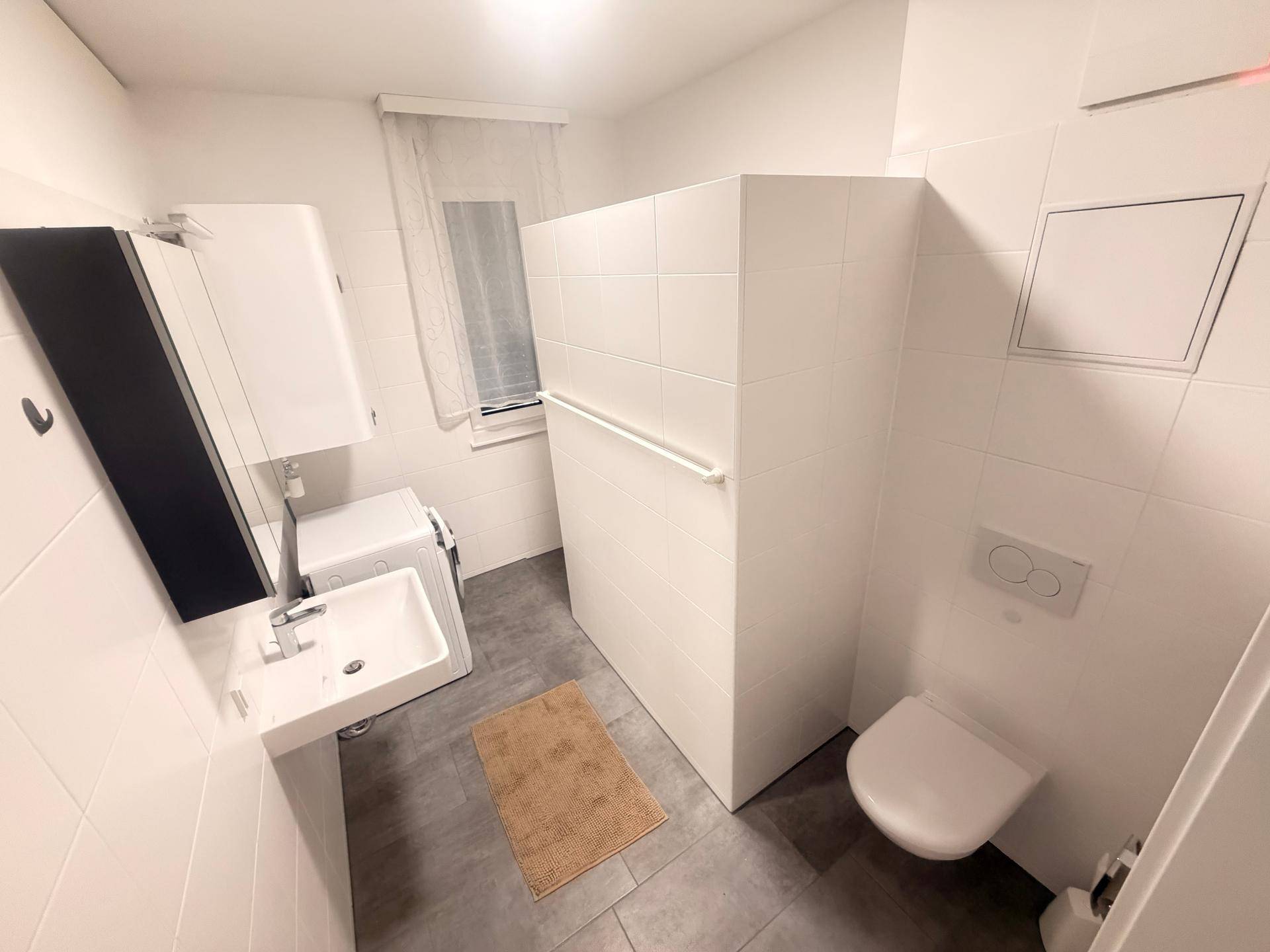 Modernes Badezimmer mit weißen Fliesen, Waschbecken und wandhängendem WC.