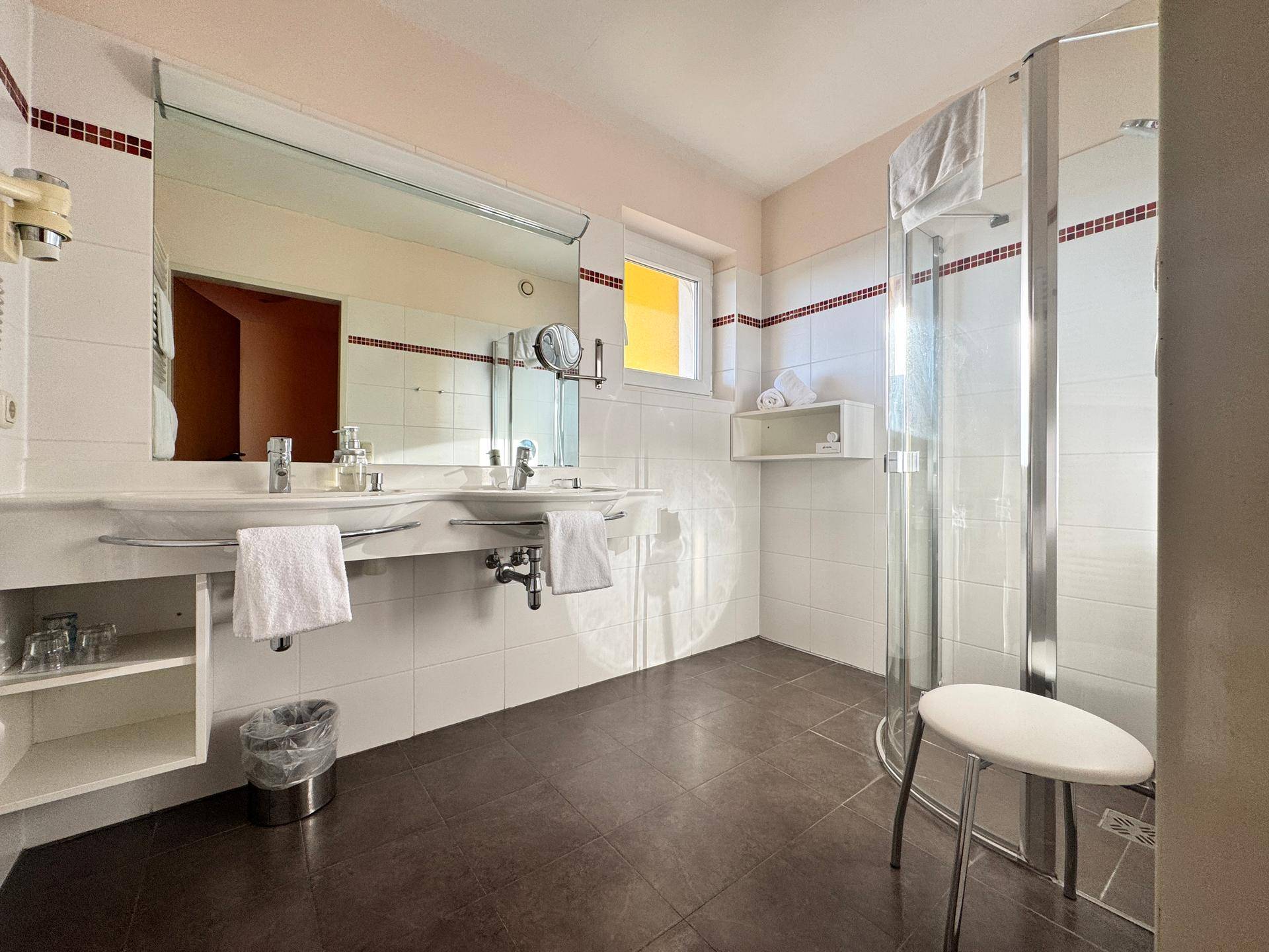 Badezimmer mit Doppelwaschbecken, Duschkabine und Fenster.