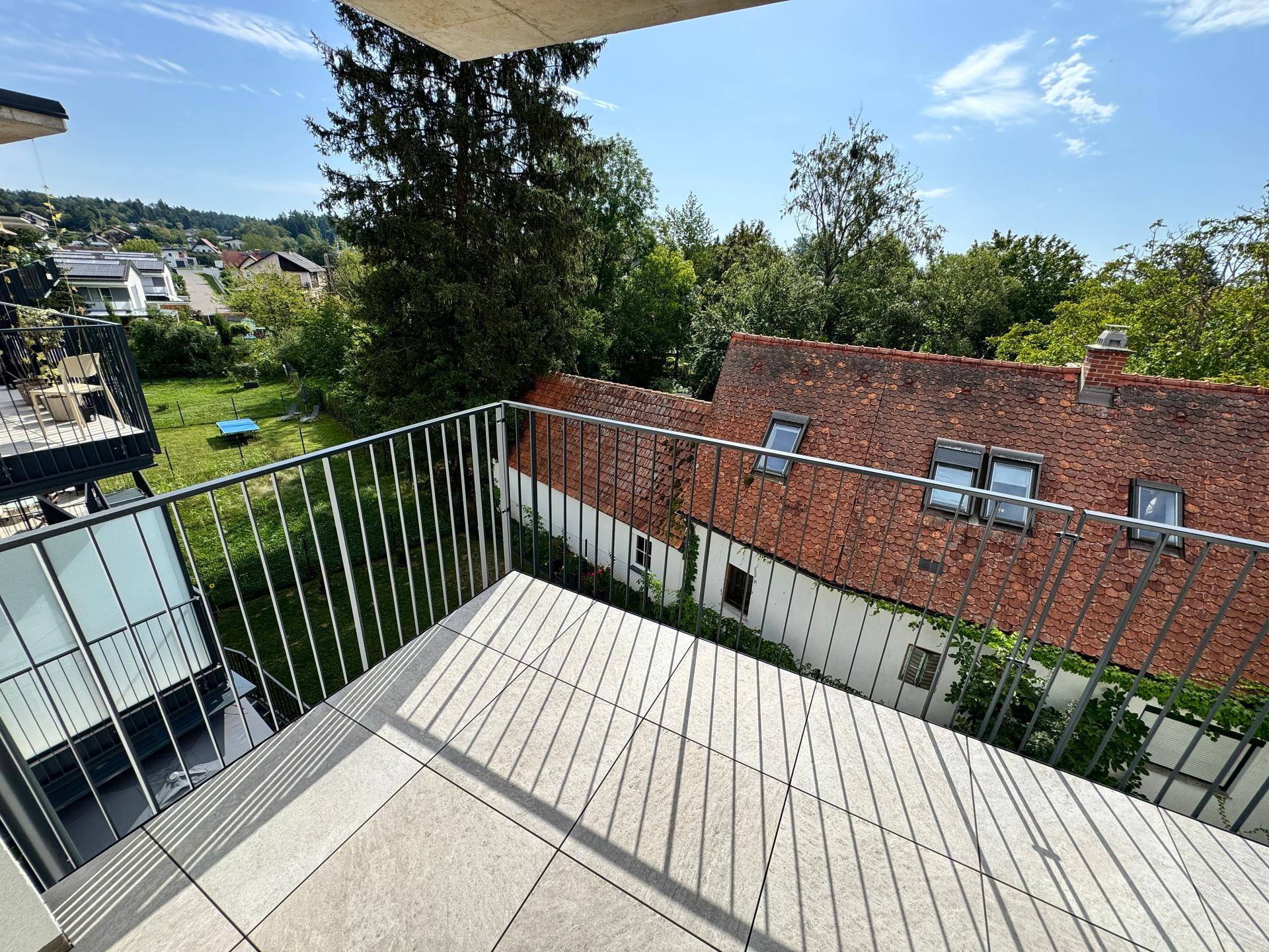 Geräumiger Balkon mit Fliesenboden und Metallgeländer, bietet einen weiten Blick ins Grüne.