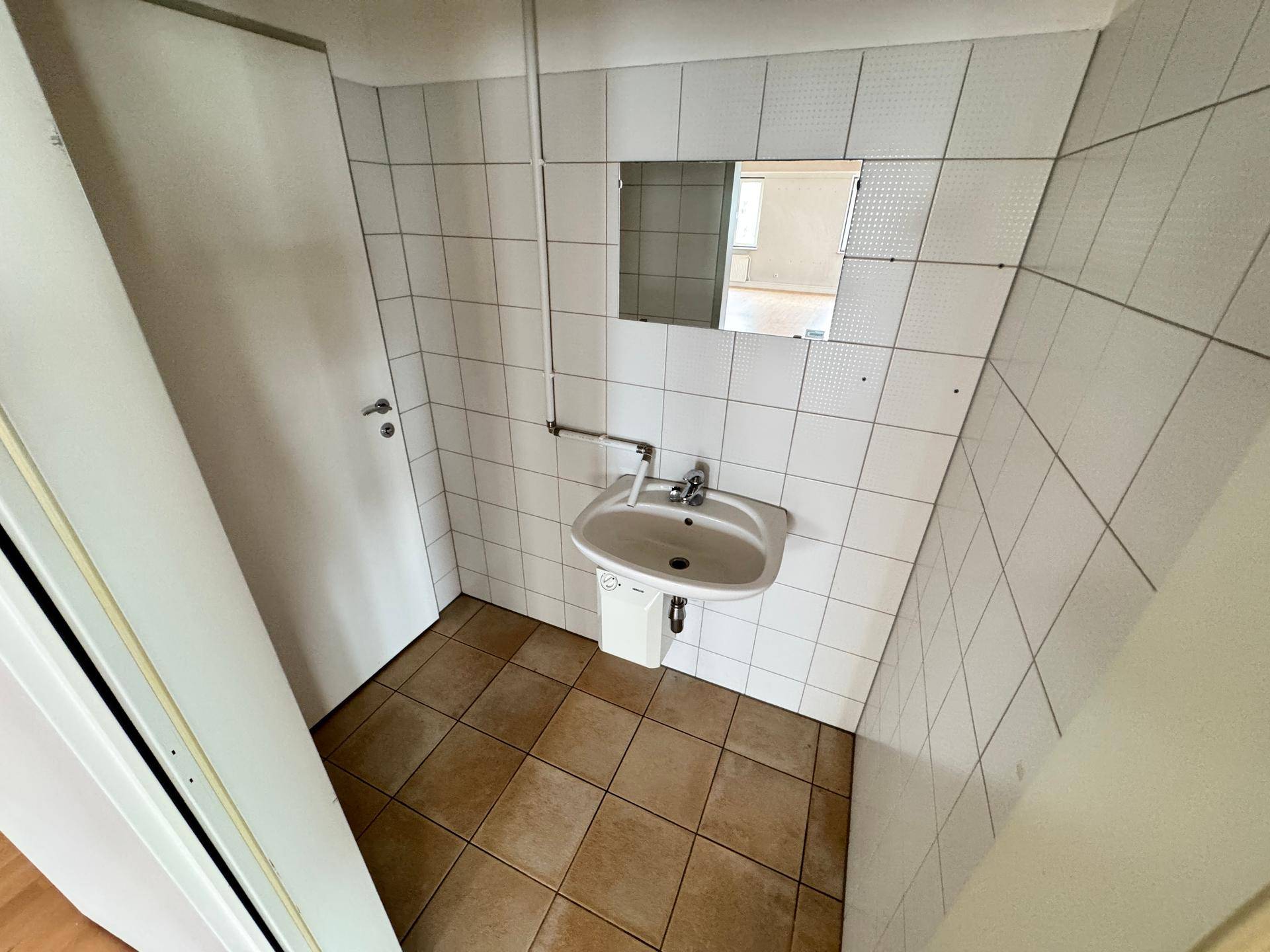 Einfaches Badezimmer mit Einzelwaschbecken, Spiegel und weißen Wandfliesen.