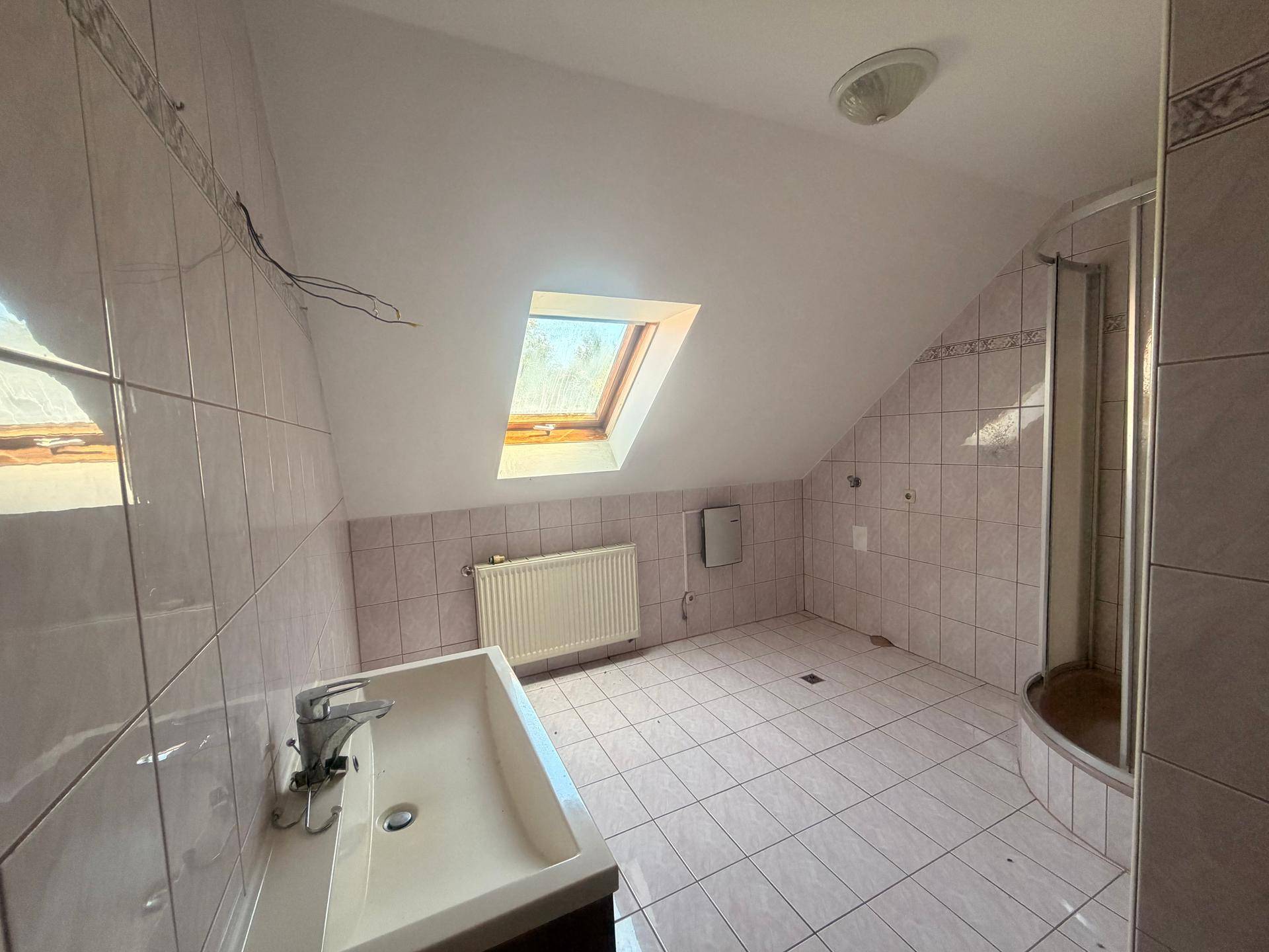 Badezimmer im Dachgeschoss mit Dachfenster, Fliesen und Duschkabine.