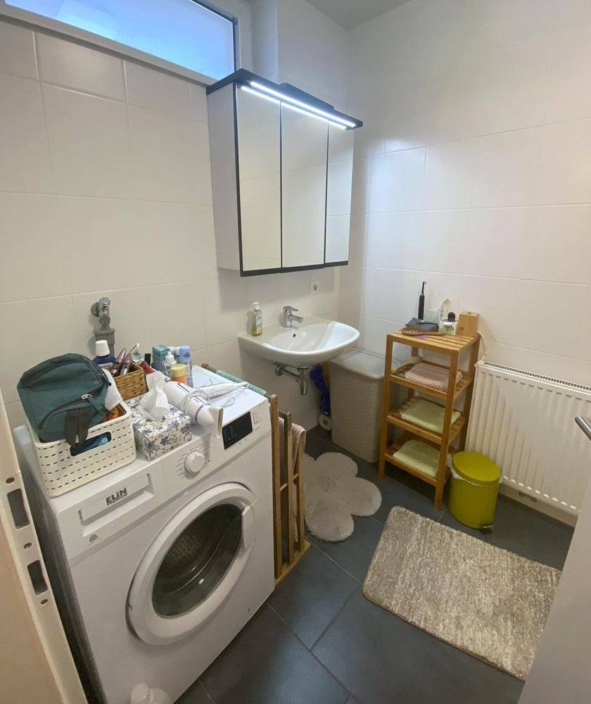 Helles Badezimmer mit Waschbecken, Waschmaschine und Fenster.