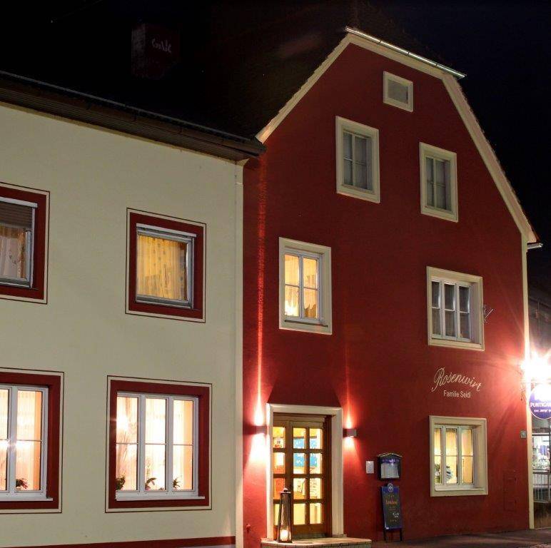 Rotes Gebäude mit beleuchtetem Eingangsbereich und Fenstern bei Nacht.