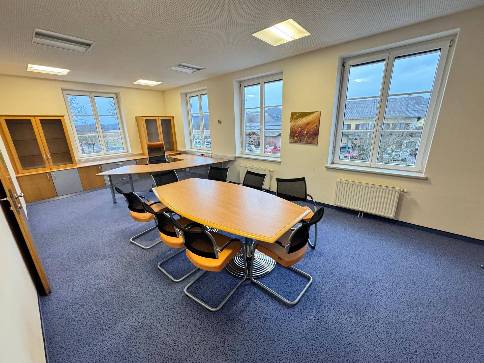 Geräumiger Büroraum mit blauem Teppichboden, Konferenztisch und großen Fenstern.