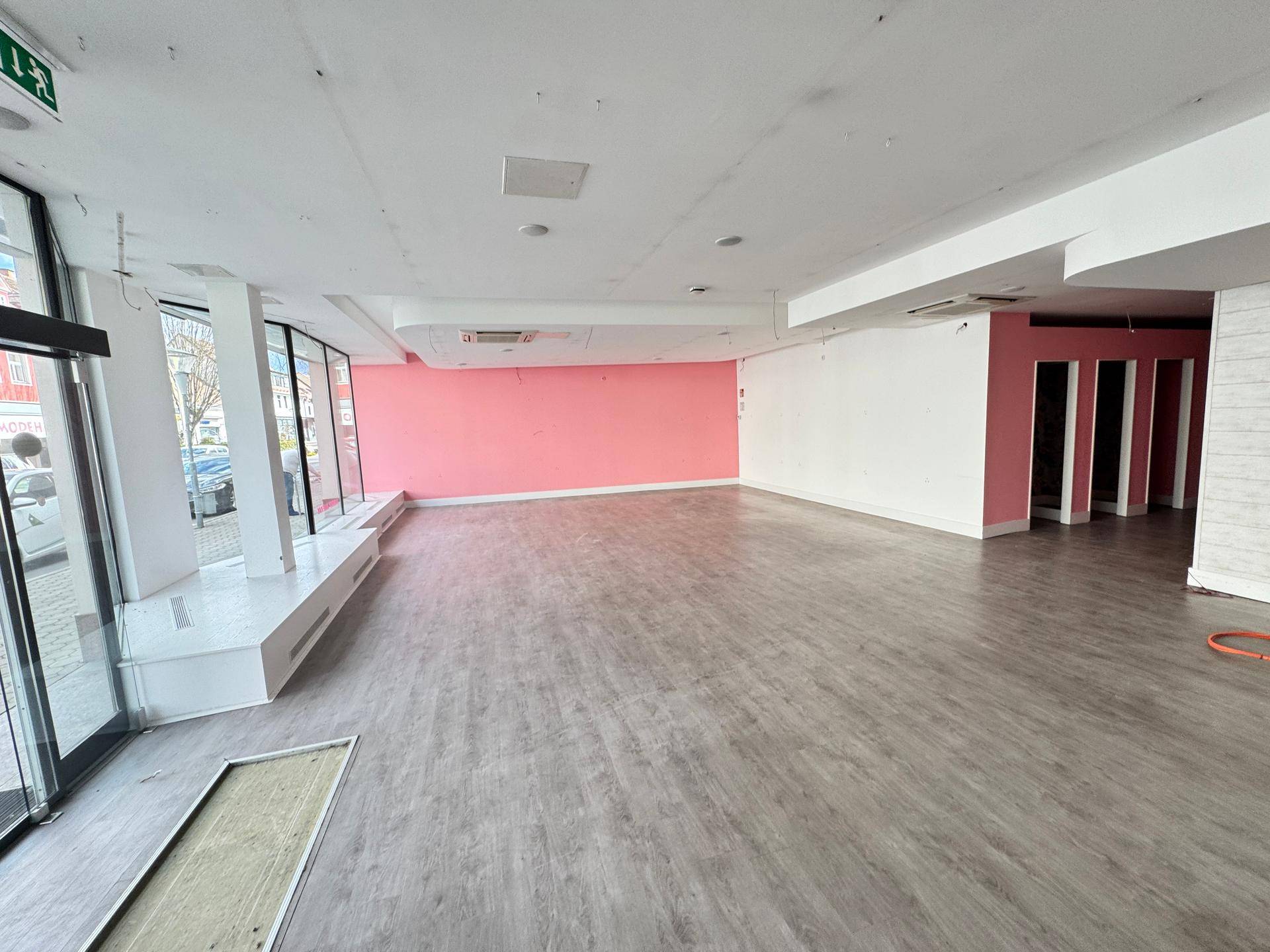 Heller Verkaufsraum mit Laminatboden, rosa Wänden und großen Schaufenstern.