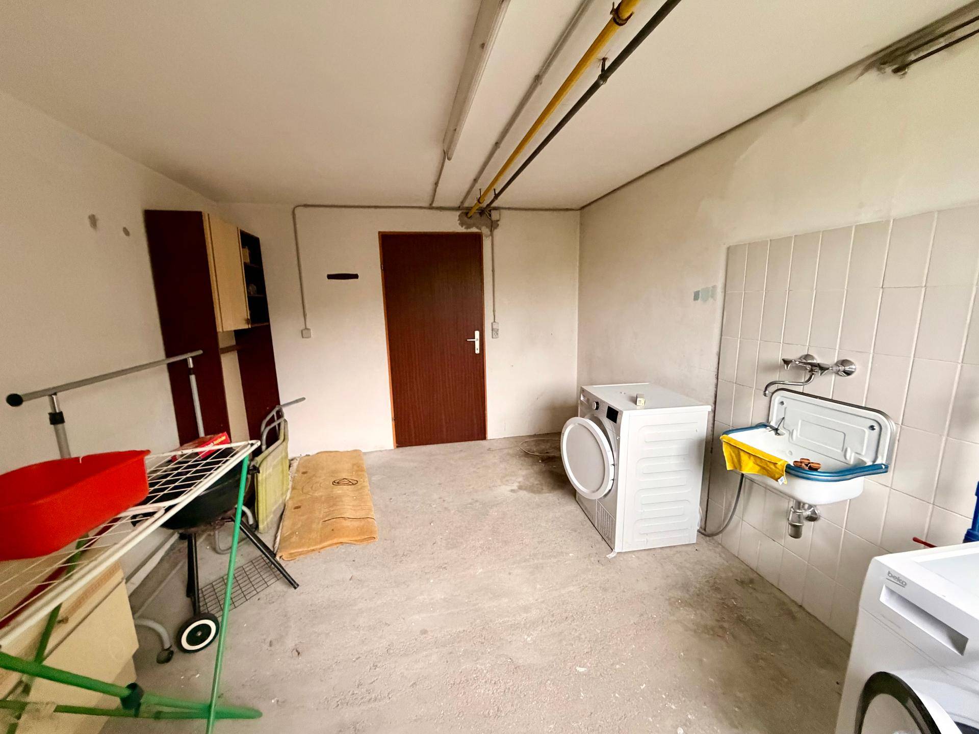 Funktionale Waschküche im Keller mit Waschbecken und Platz für Wäschepflege.