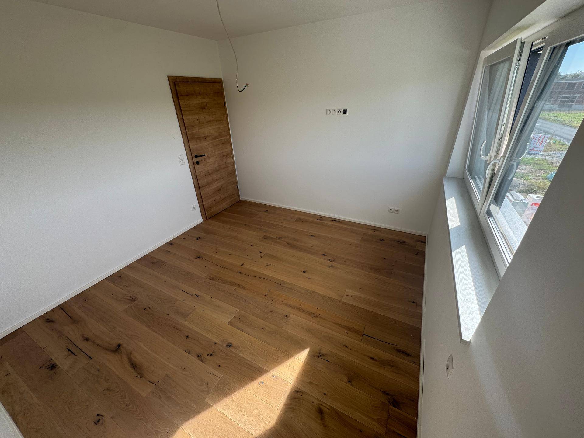 Schlafzimmer mit hellem Eichenparkett, weißen Wänden und Fenster.