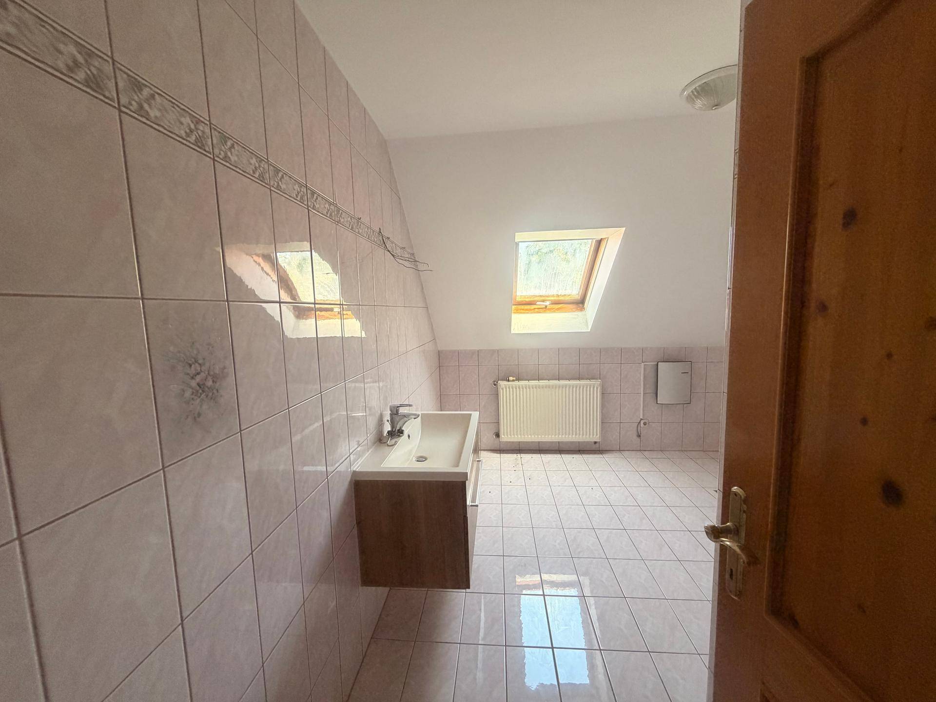 Badezimmer mit Waschbecken, rosa Fliesen, Dachschräge und Dachfenster für natürliches Licht.