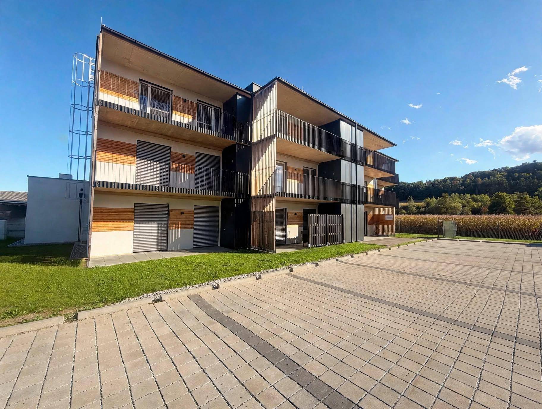 Neubau-Mehrfamilienhaus mit moderner Architektur, Balkonen und gepflasterten Parkflächen.