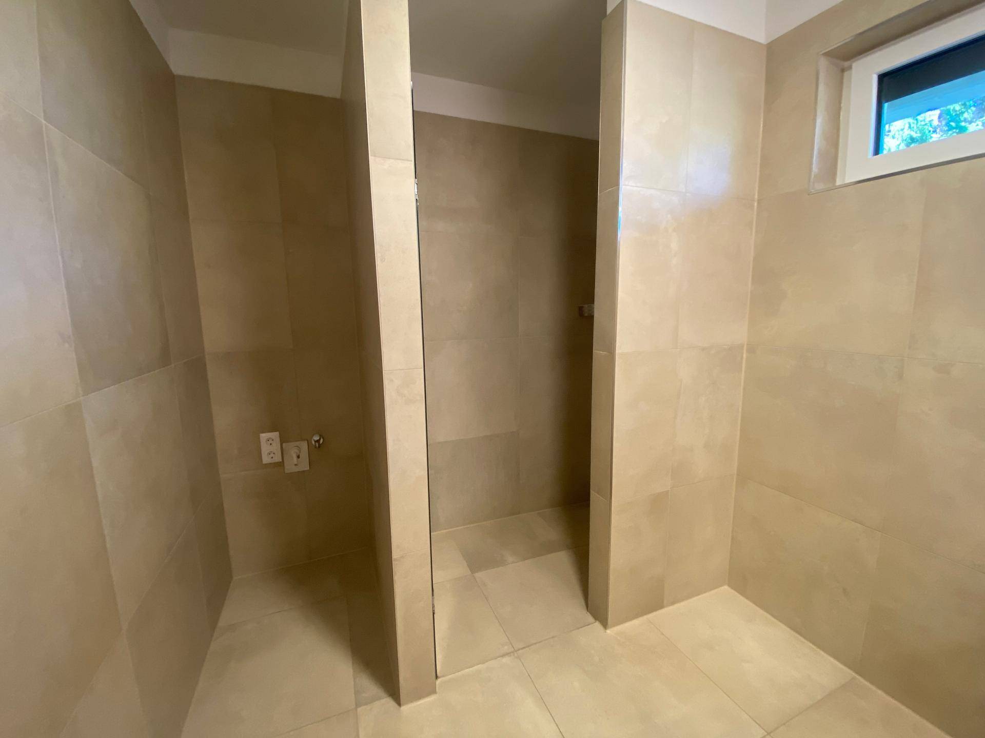Geräumiges Badezimmer mit beigefarbenen Fliesen und vorbereitetem Bereich für eine Dusche.