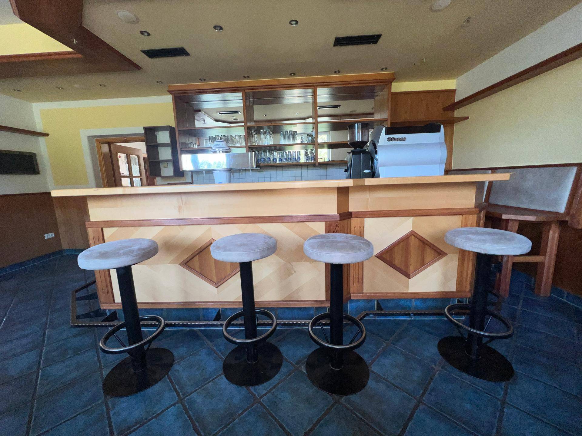 Frontansicht der Bar mit vier Barhockern und Holzverkleidung, bereit für Gäste.