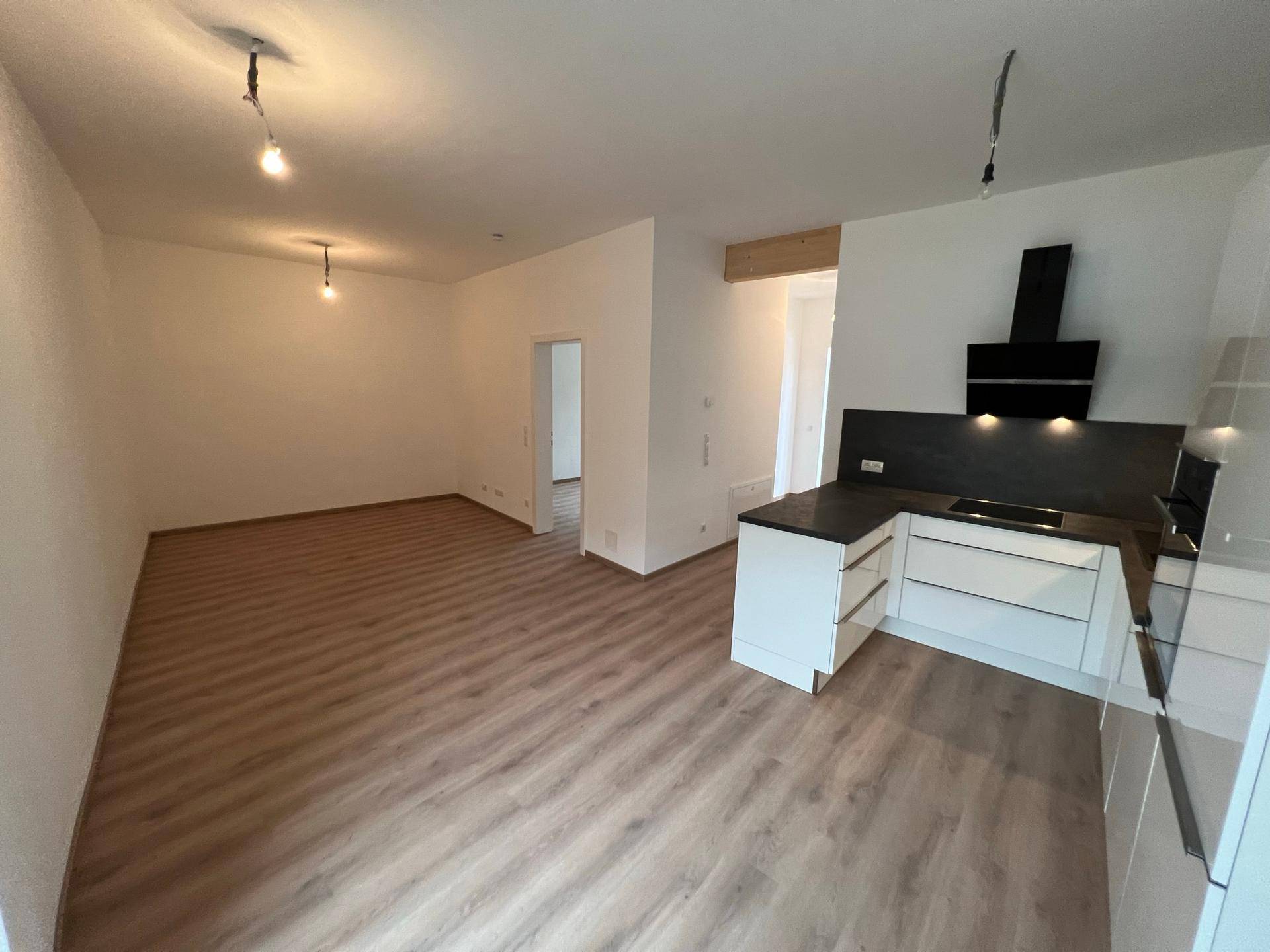 Offener Wohnbereich mit vorbereiteter Küchenzeile und Laminatboden, bereit zur individuellen Gestaltung.