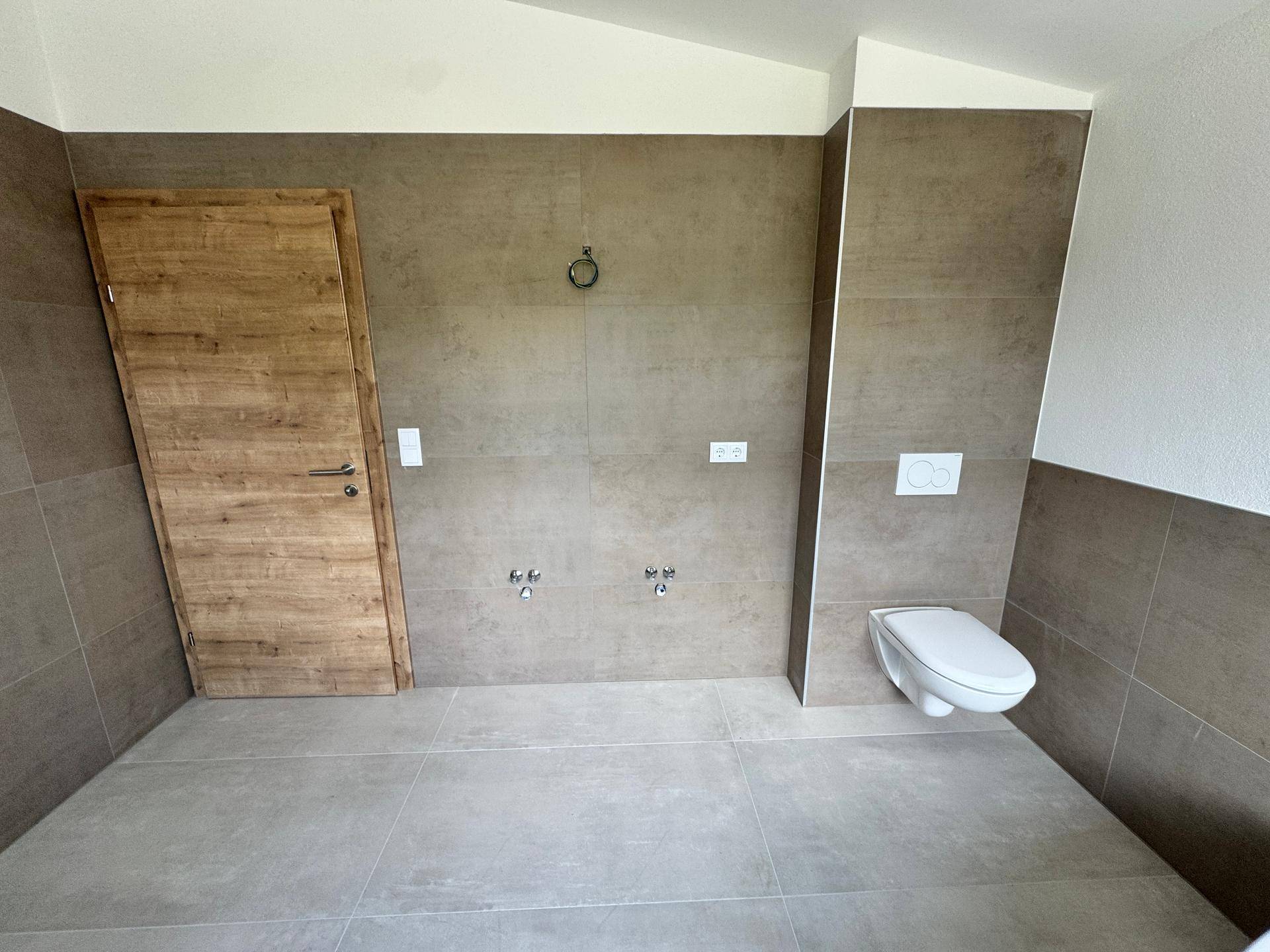 Badezimmer mit Holztür, wandhängendem WC und Vorbereitung für einen Doppelwaschtisch.