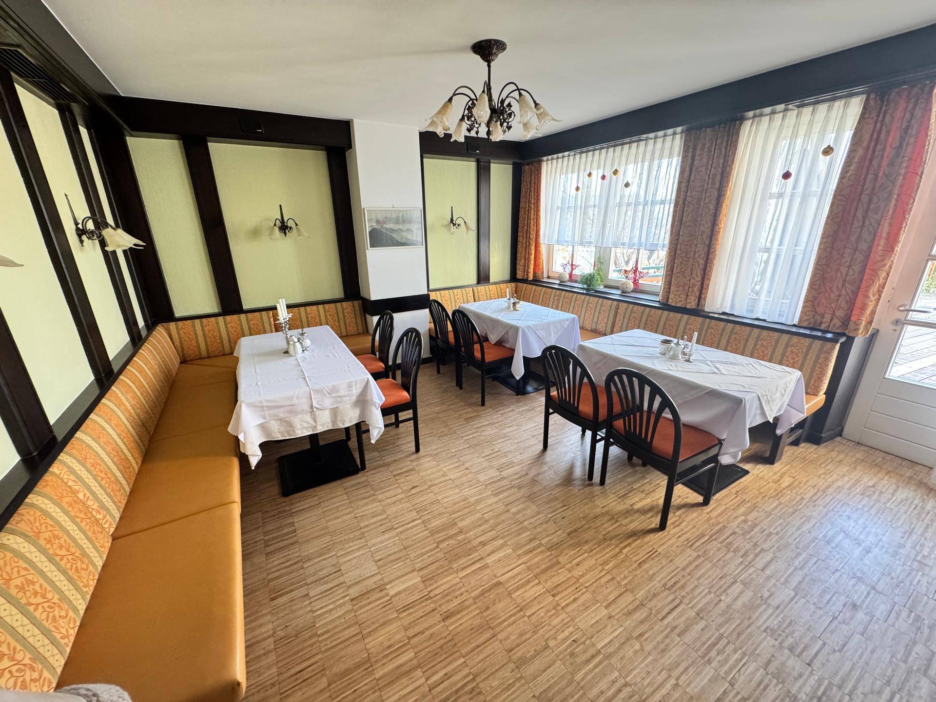 Heller Essbereich mit Sitzbänken, Tischen und Parkettboden.