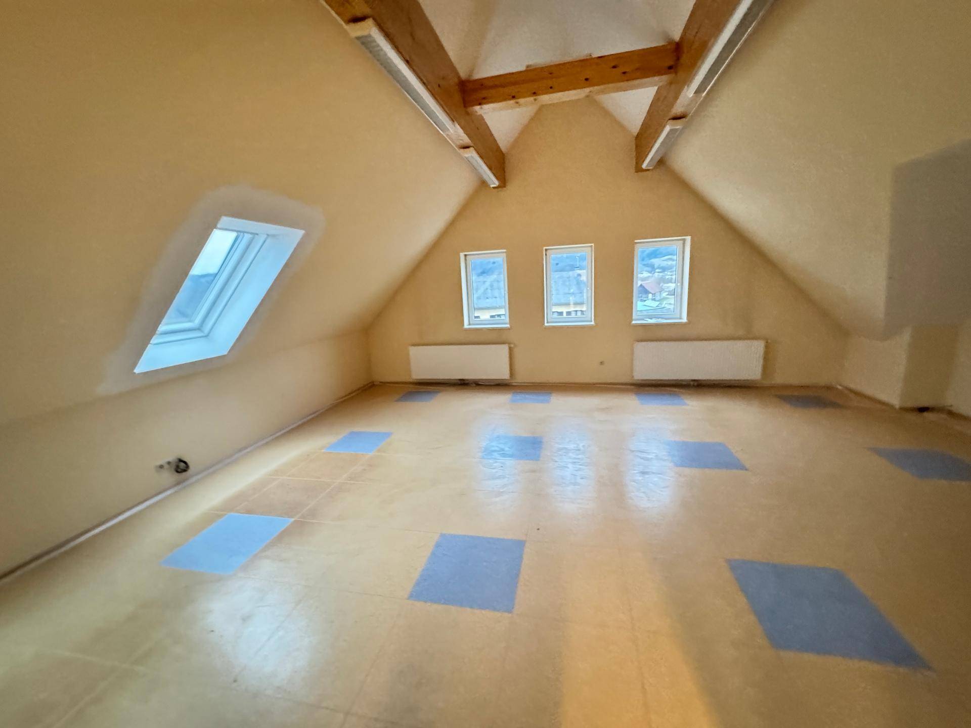 Geräumiger Dachbodenraum mit sichtbaren Holzbalken, Dachfenster und farbigem Bodenbelag.
