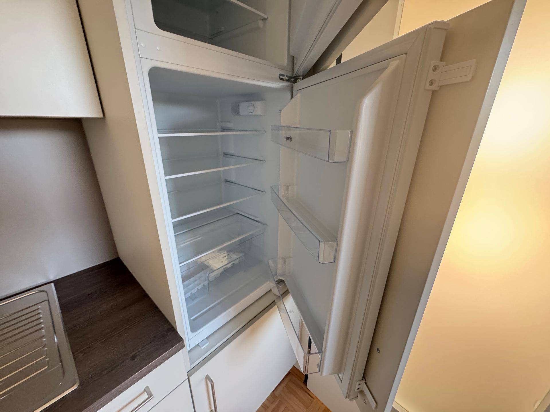 Offener Kühlschrank mit mehreren Ablagefächern in einer Einbauküche.