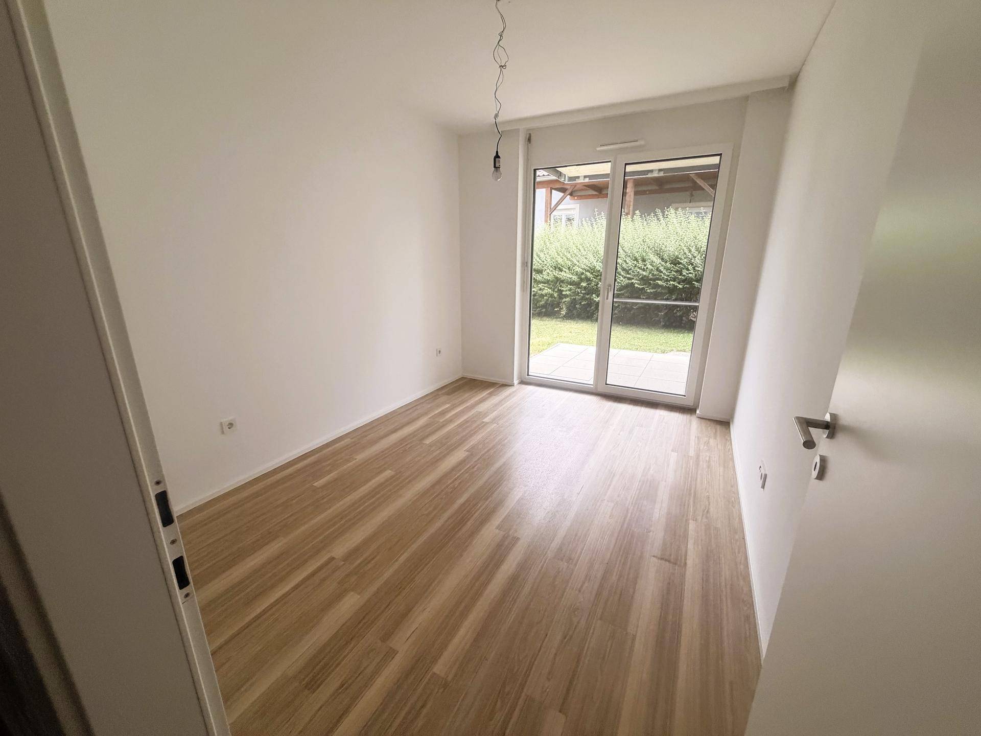 Helles Zimmer mit Laminatboden und großen Fenstern zum Garten.