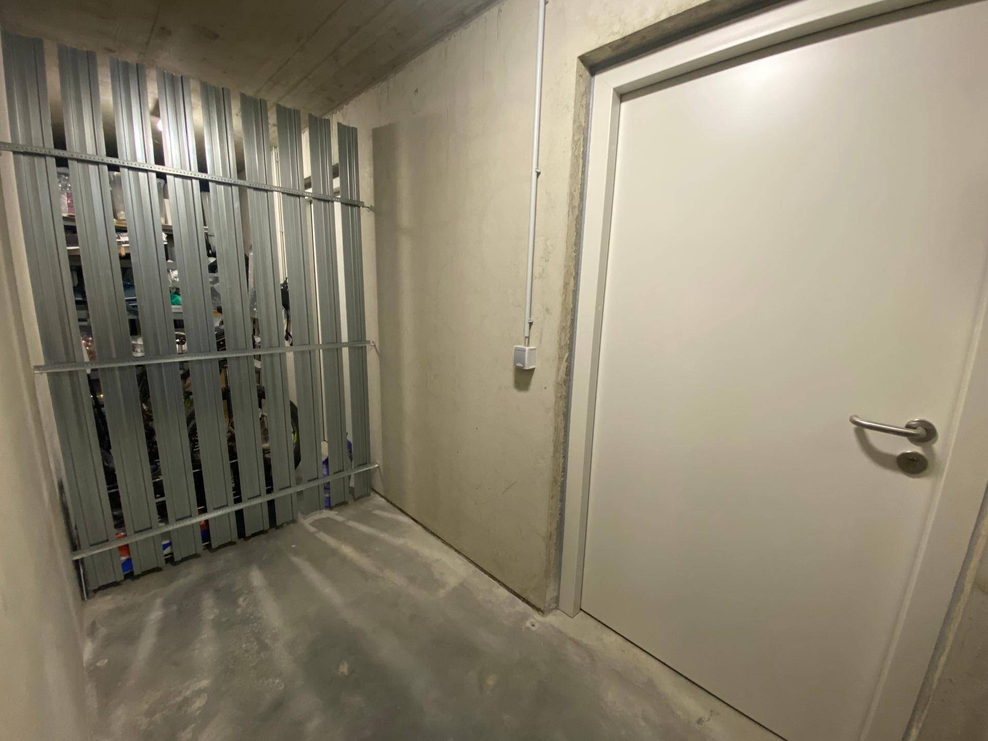 Kellerabteil mit Metallabtrennung und Betonboden, ideal für zusätzlichen Stauraum.