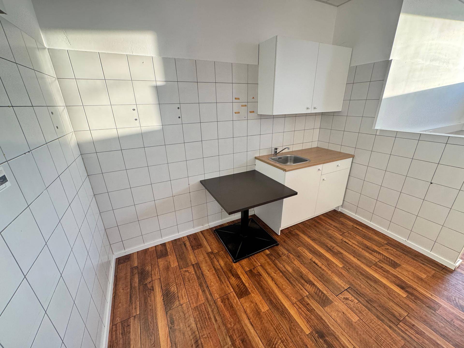 Kleine Küchenzeile mit Spüle, Unterschrank und einem Tisch, ideal für eine Teeküche.