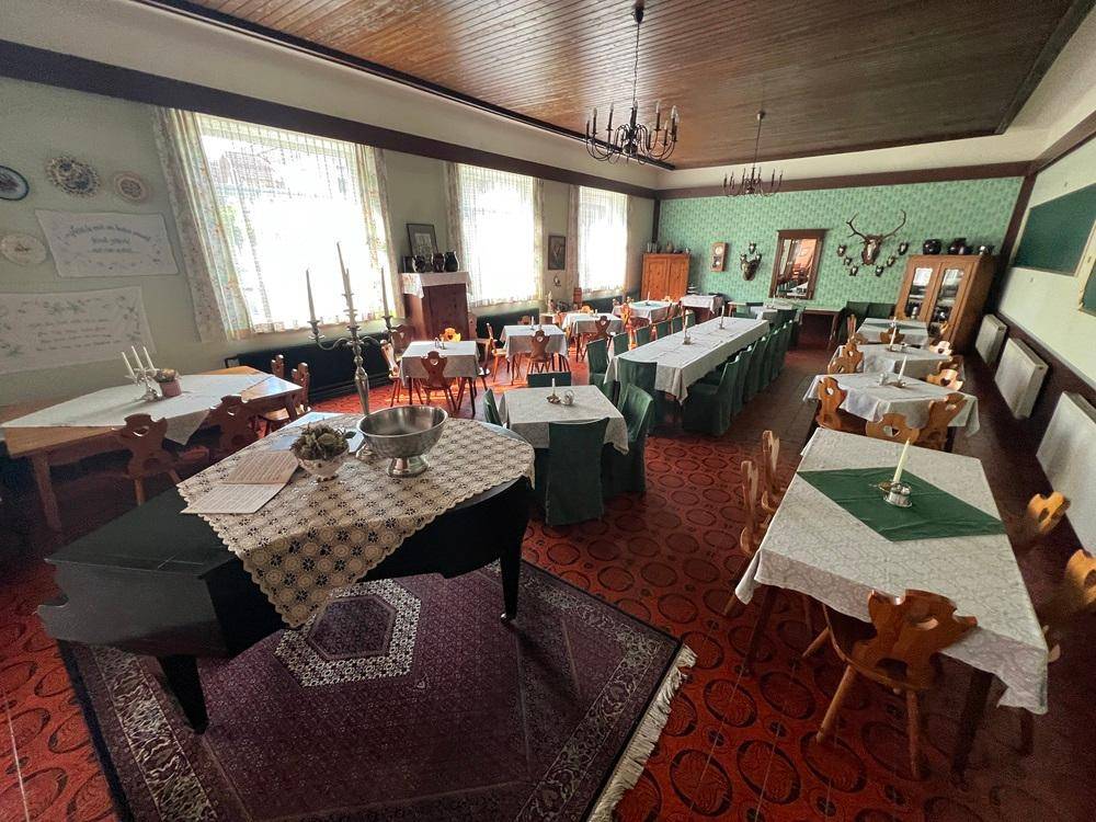 Großer Speisesaal mit vielen Tischen, Stühlen, einem Flügel und traditioneller Dekoration.