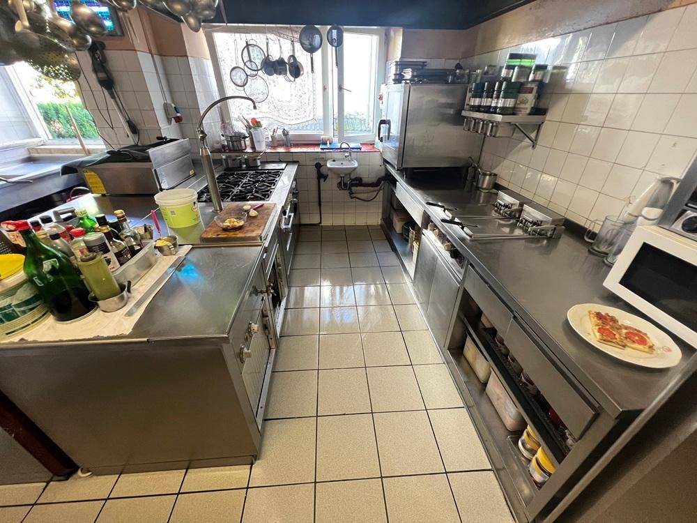 Professionelle Küche mit Gasherd, modernen Edelstahlgeräten und Fliesenboden.